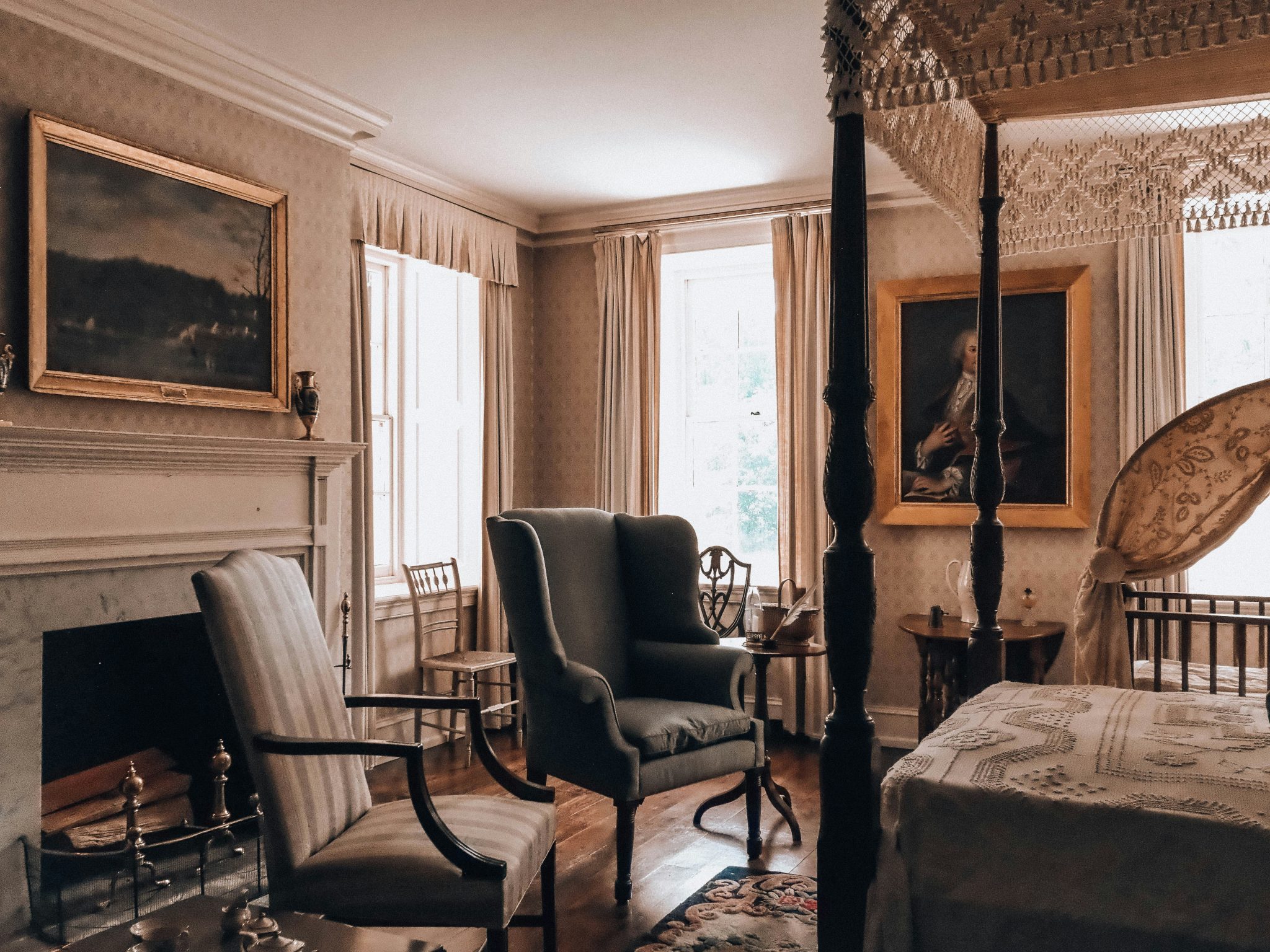 A vintage bedroom with a four-poster bed, fireplace, and armchairs.