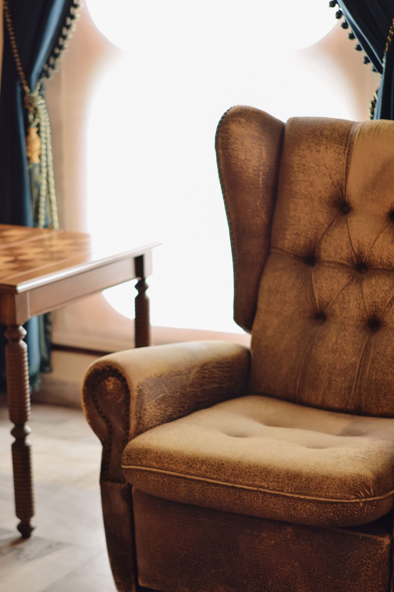 A vintage leather armchair beside a chessboard table in a tastefully decorated room.