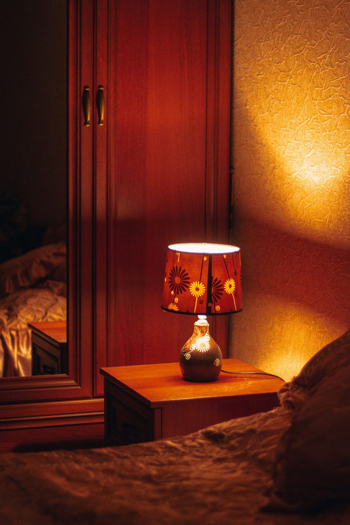 A warm and inviting bedroom scene featuring a lamp on a wooden bedside table, emitting a soft glow.