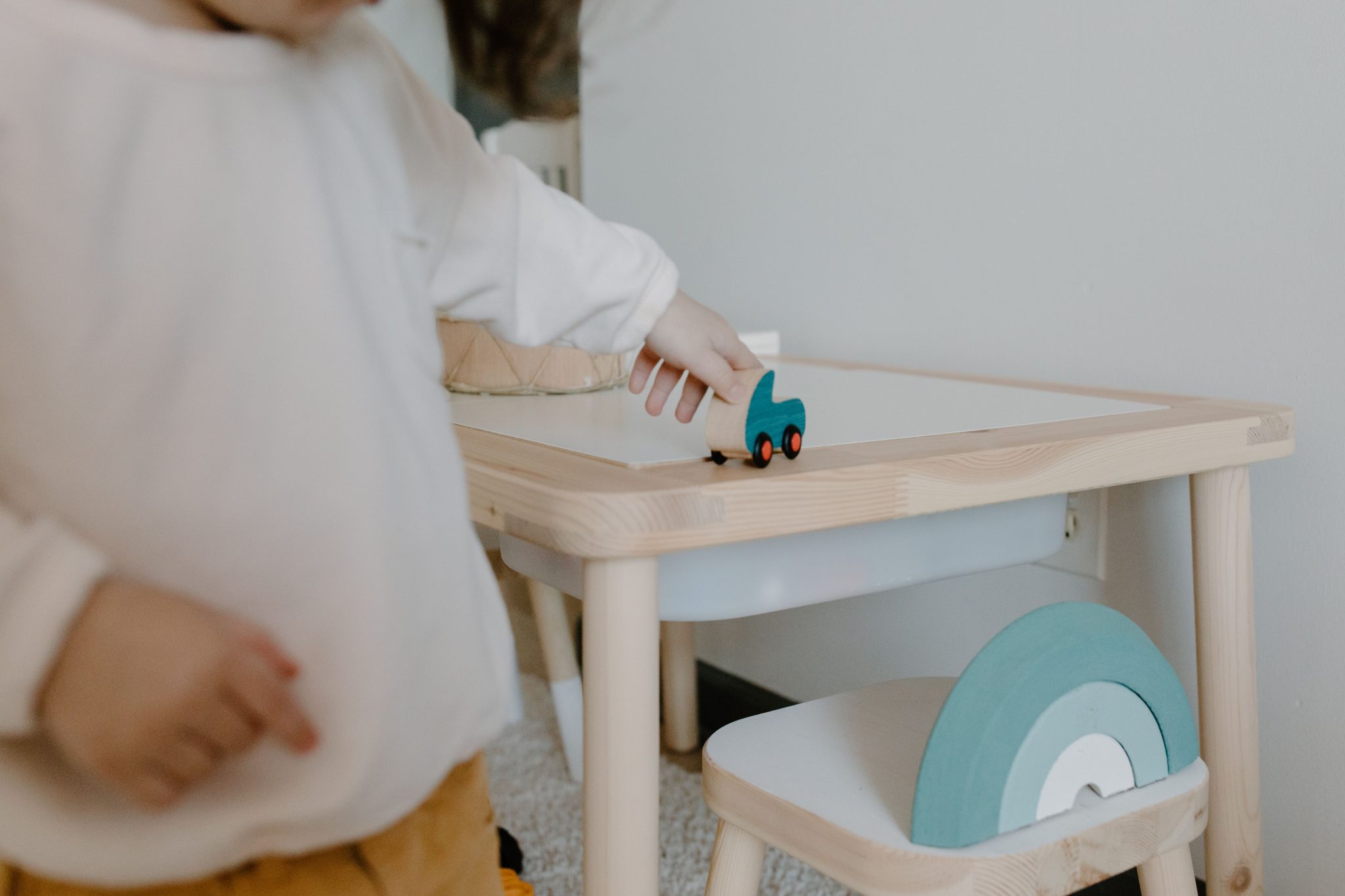 A young child plays with a wooden toy on a small table indoors, showcasing minimalist design.