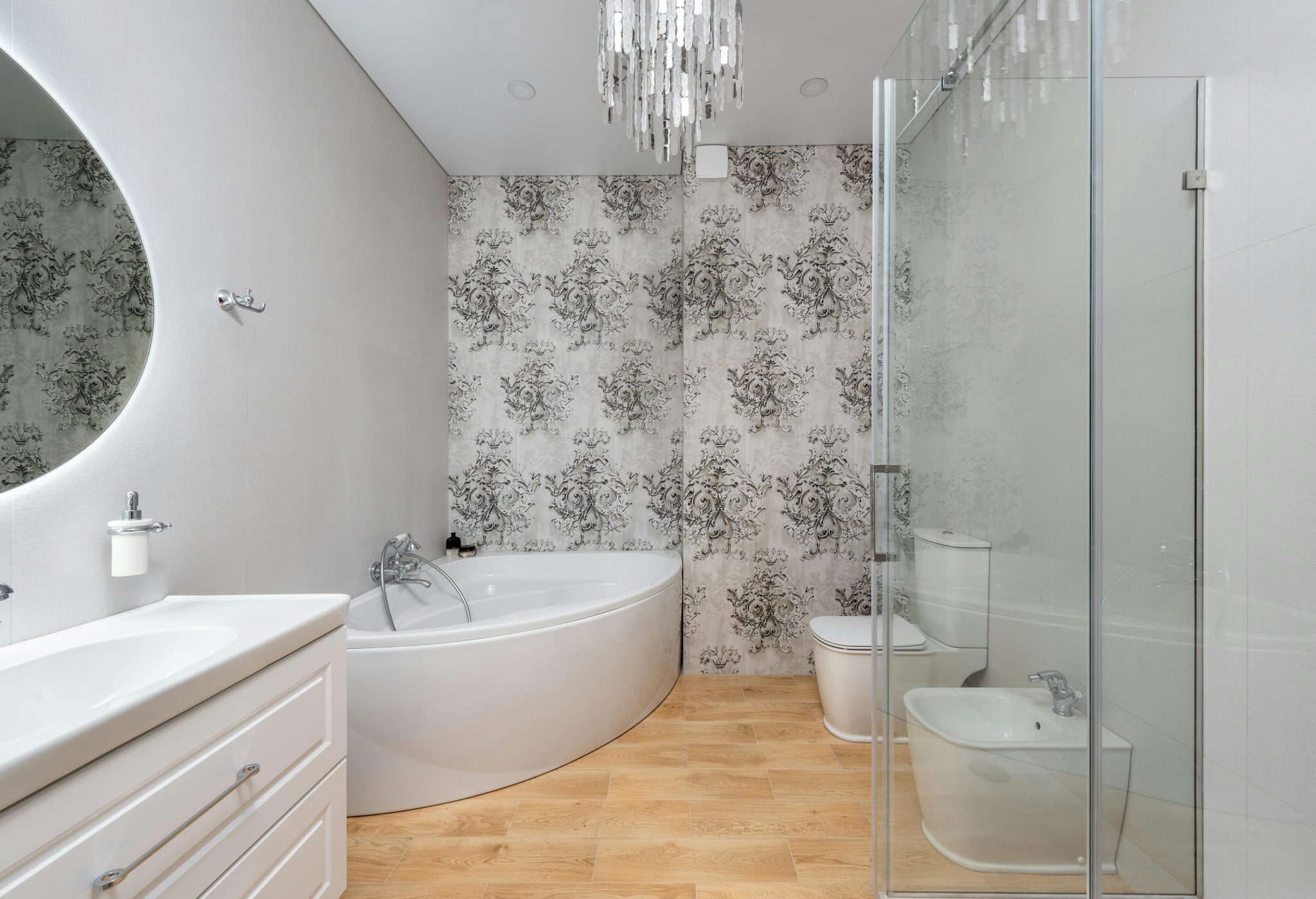 Bath against bidet and mirror above washstand in contemporary bathroom with chandelier and ornamental wall in house