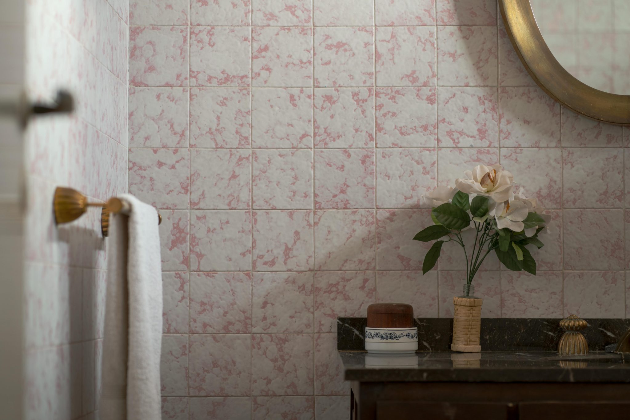 Charming bathroom scene with vintage tiles, a round mirror, and floral decoration.