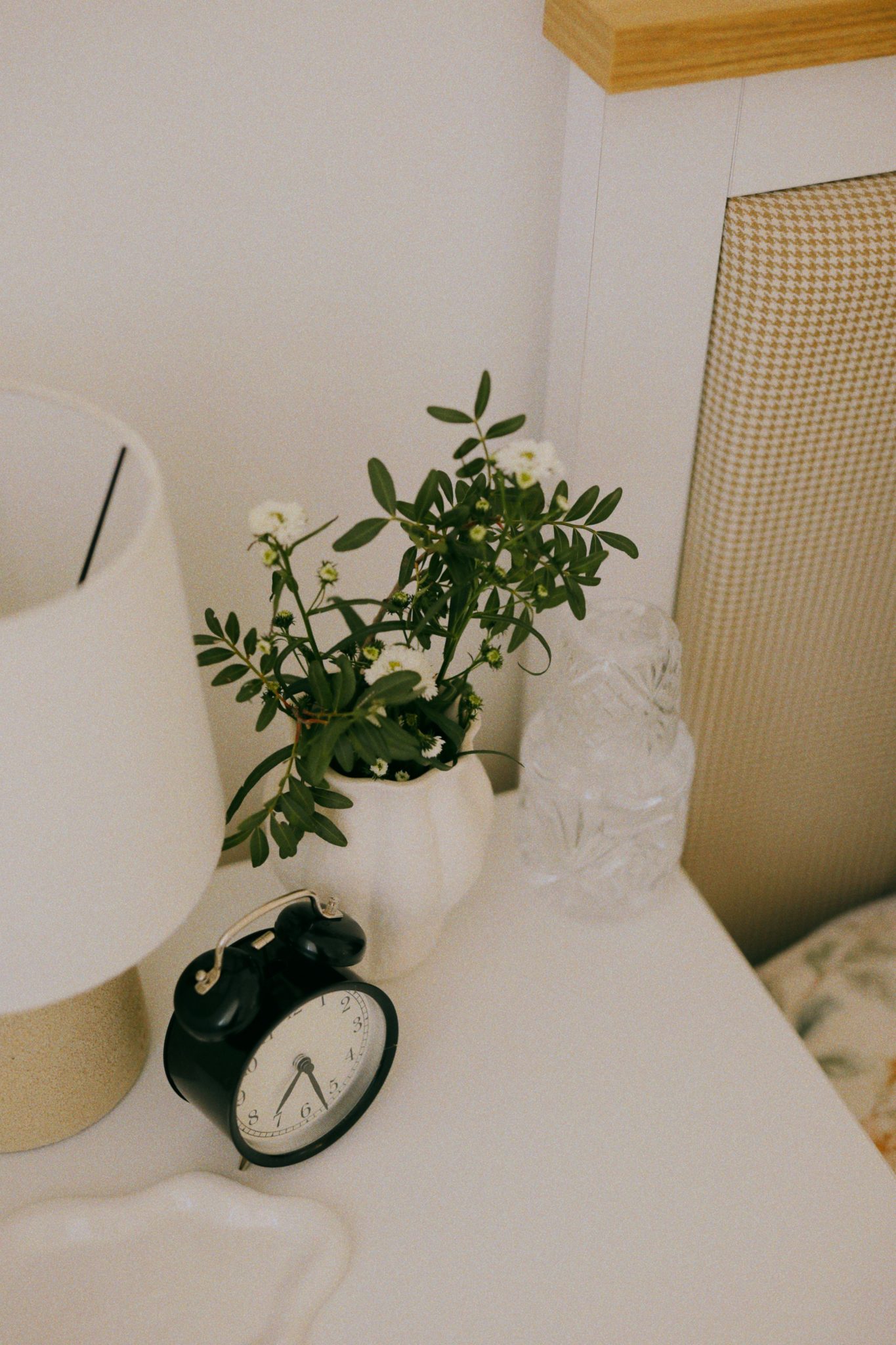 Chic nightstand featuring a classic alarm clock, vase with flowers, and lamp for a cozy ambiance.