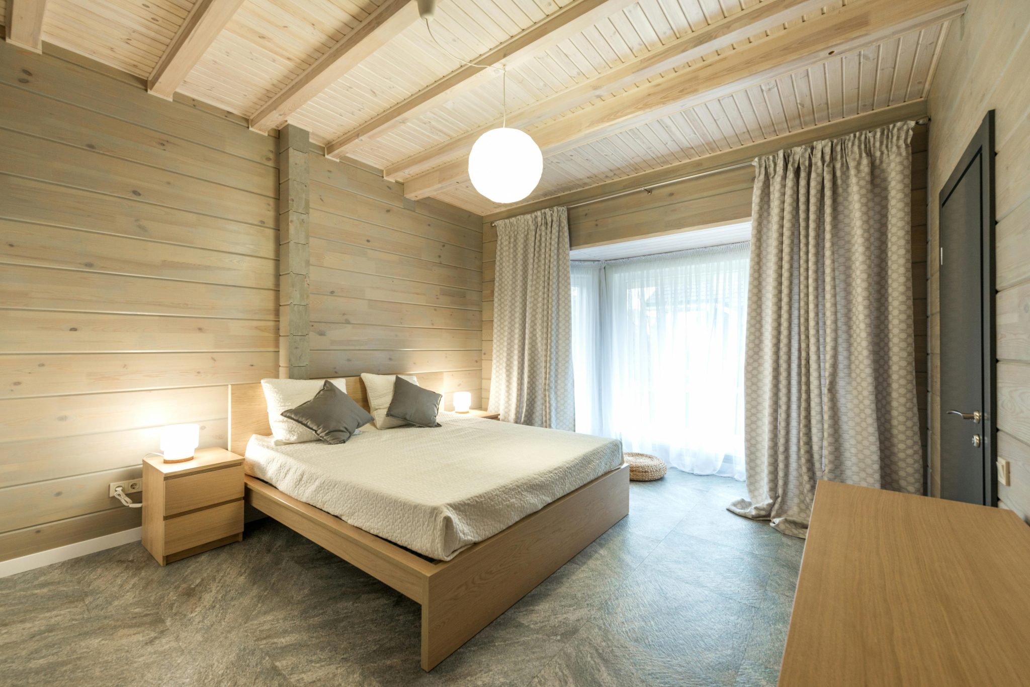 Comfortable bed with soft cushions between wooden nightstands under lamp hanging on ceiling in house