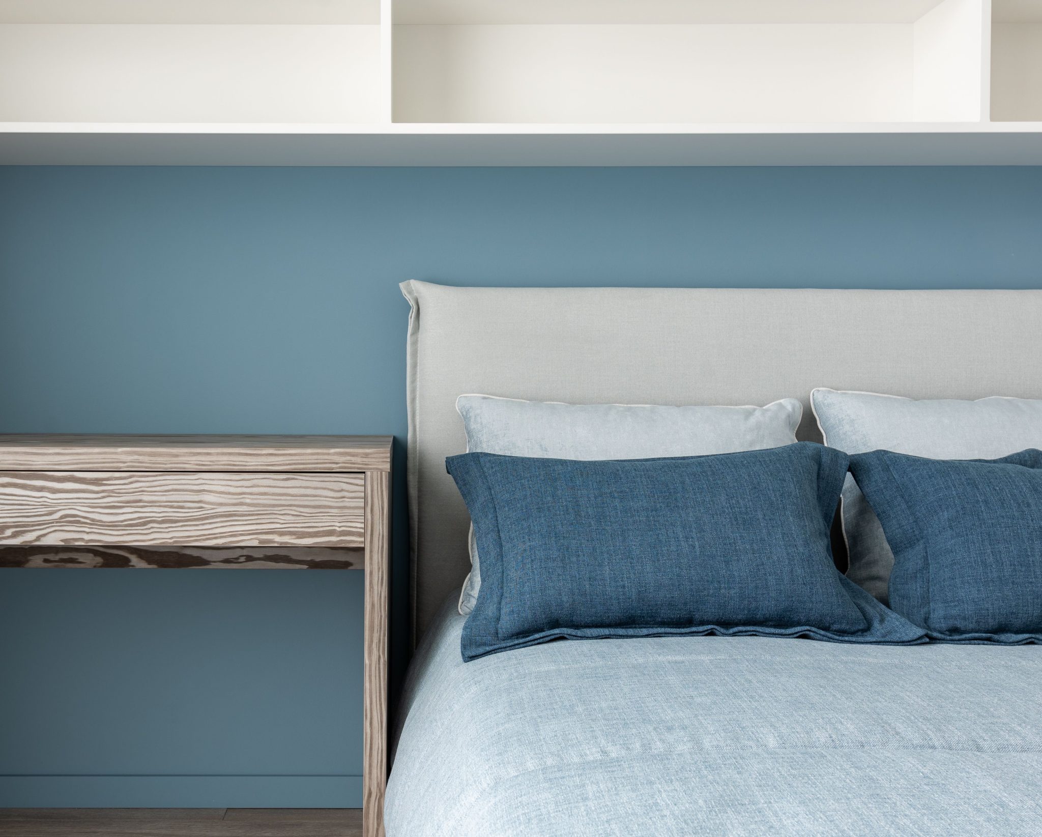 Comfortable soft bed with pillows near timber table and white shelves in contemporary bedroom