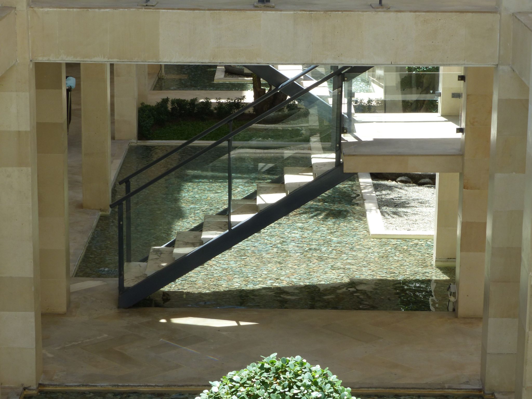 Contemporary staircase with glass railing over reflective water feature indoors.