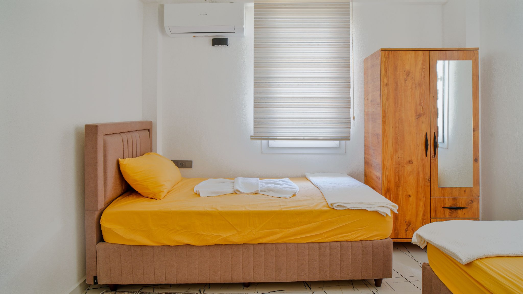 Cozy minimalist bedroom interior featuring yellow bedding, wooden wardrobe, and soft lighting.