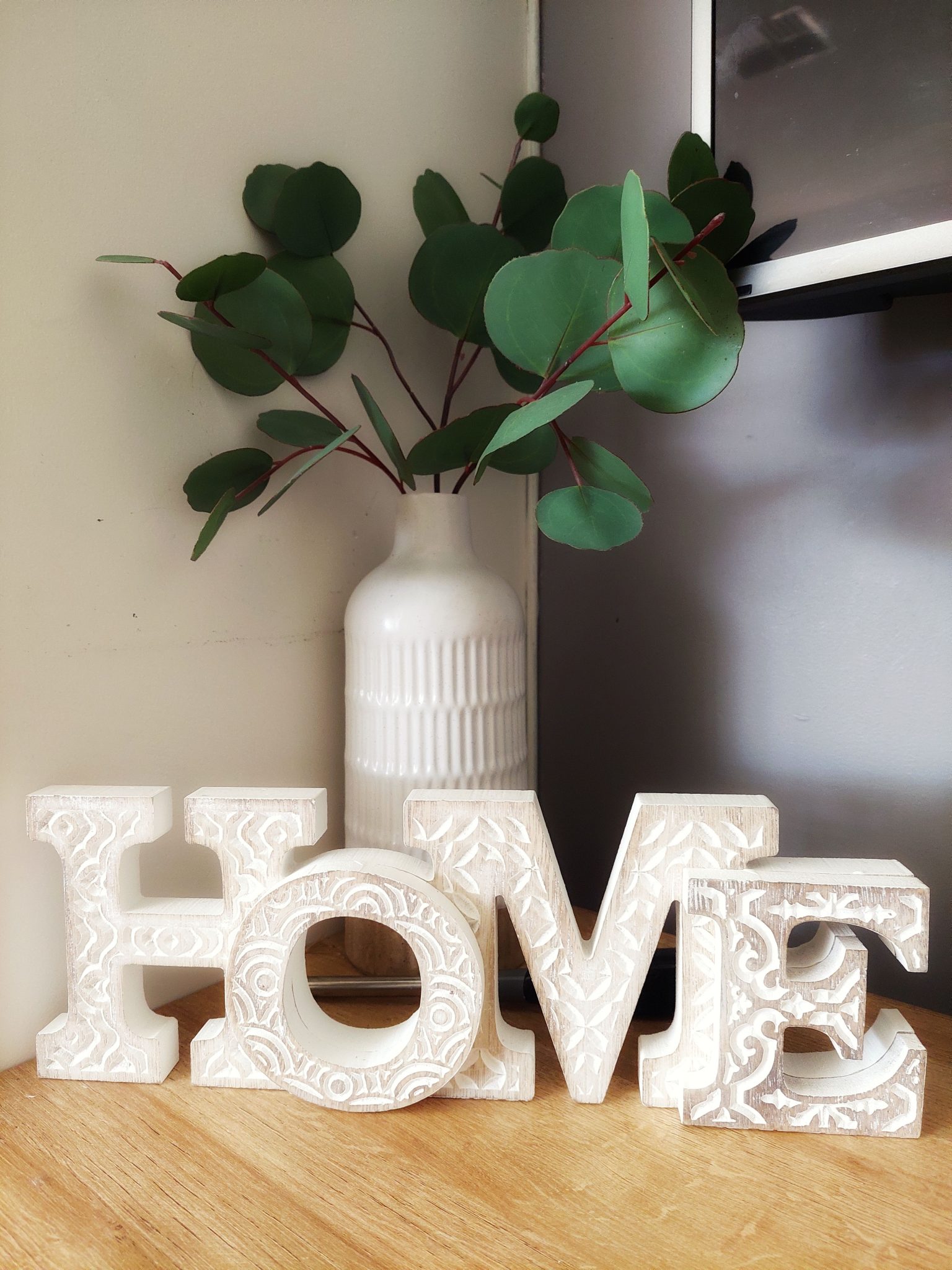 Decorative ceramic vase with green leaves and HOME letters on a wooden surface.
