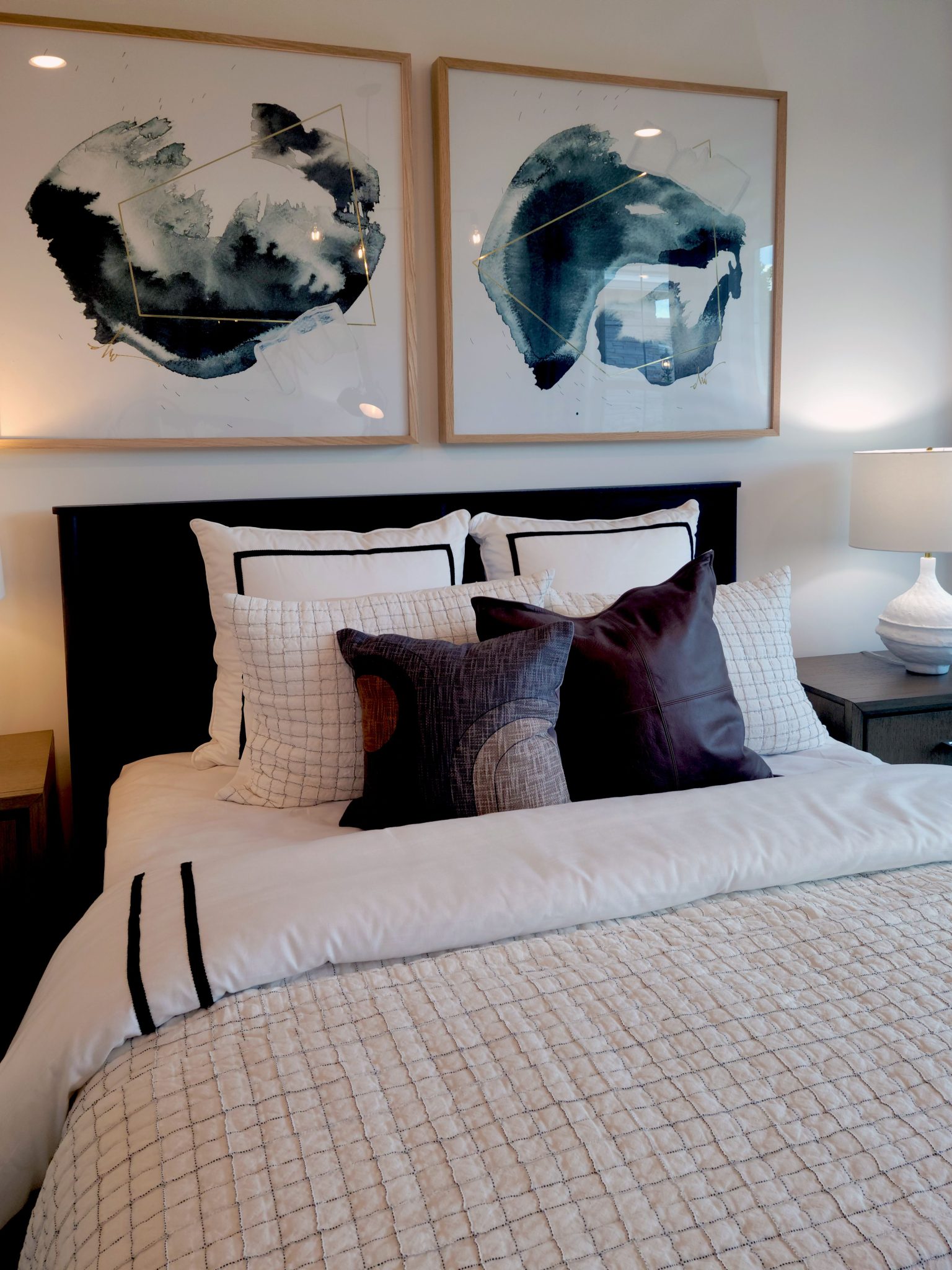 Elegant bedroom setup with abstract art above a neatly made bed, featuring decorative pillows and lamps.