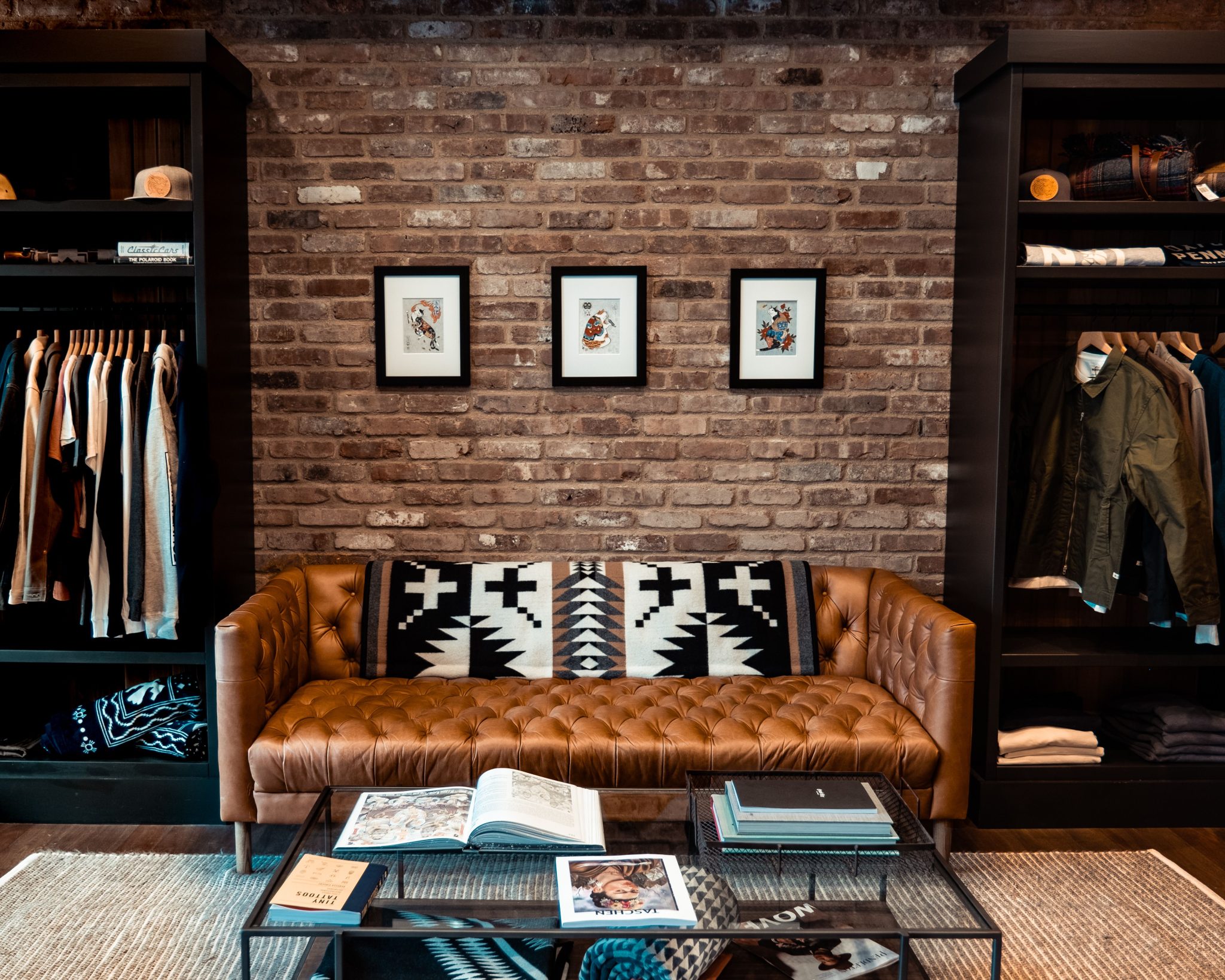 Elegant living room with brown leather couch, brick wall, art, and modern decor.
