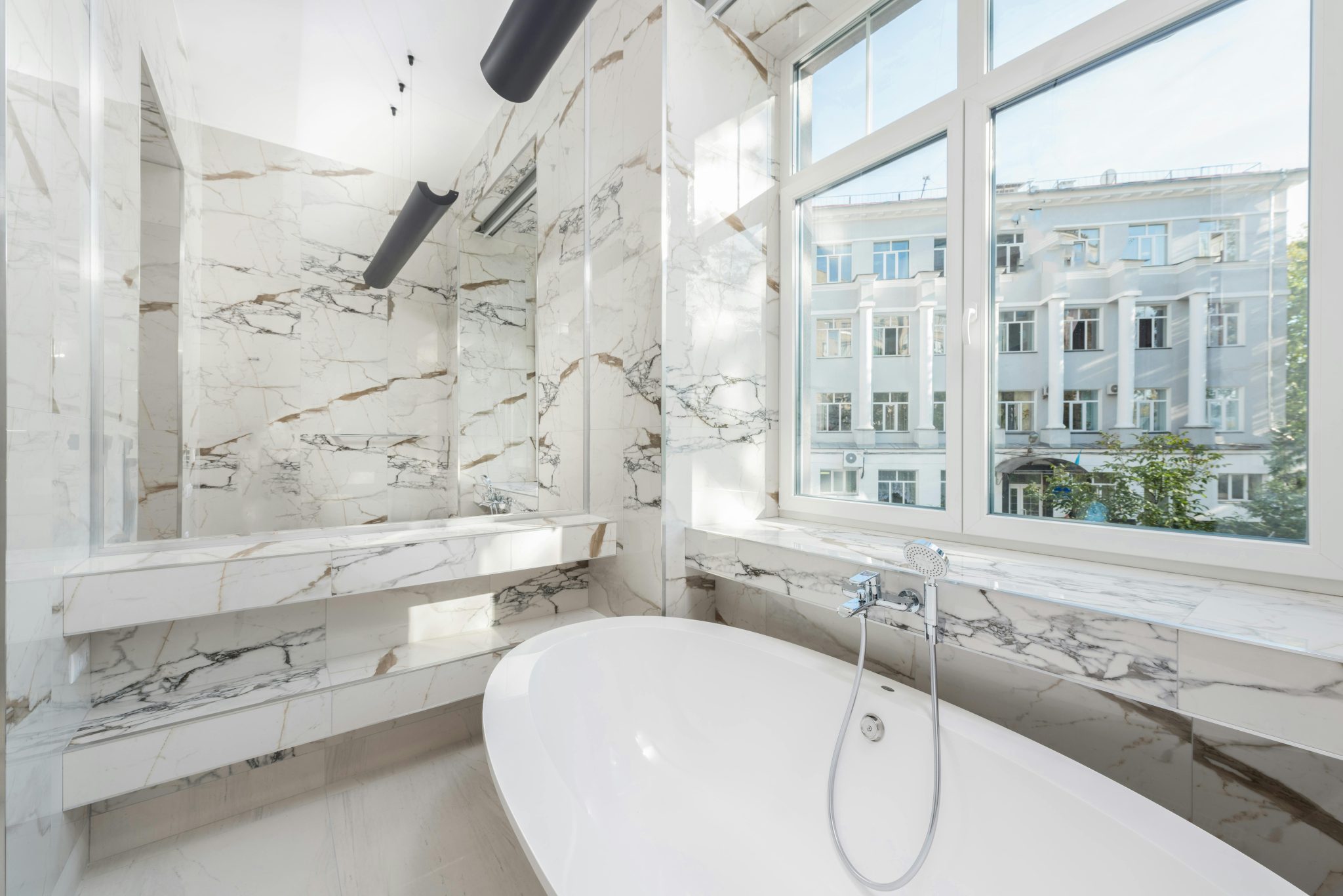 Elegant marble bathroom featuring a modern bathtub and a scenic city view.