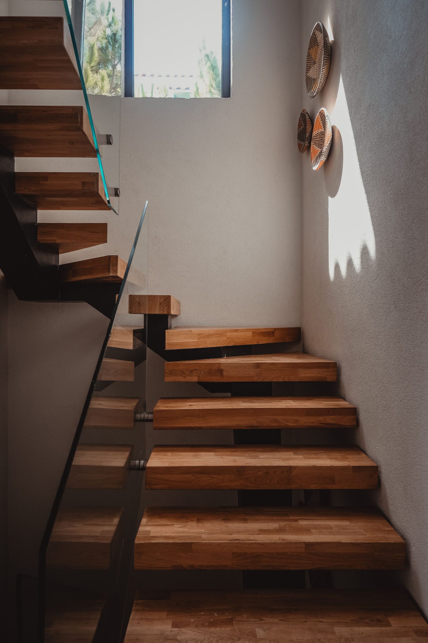 Elegant wooden staircase with glass railing in a modern rustic interior setting.