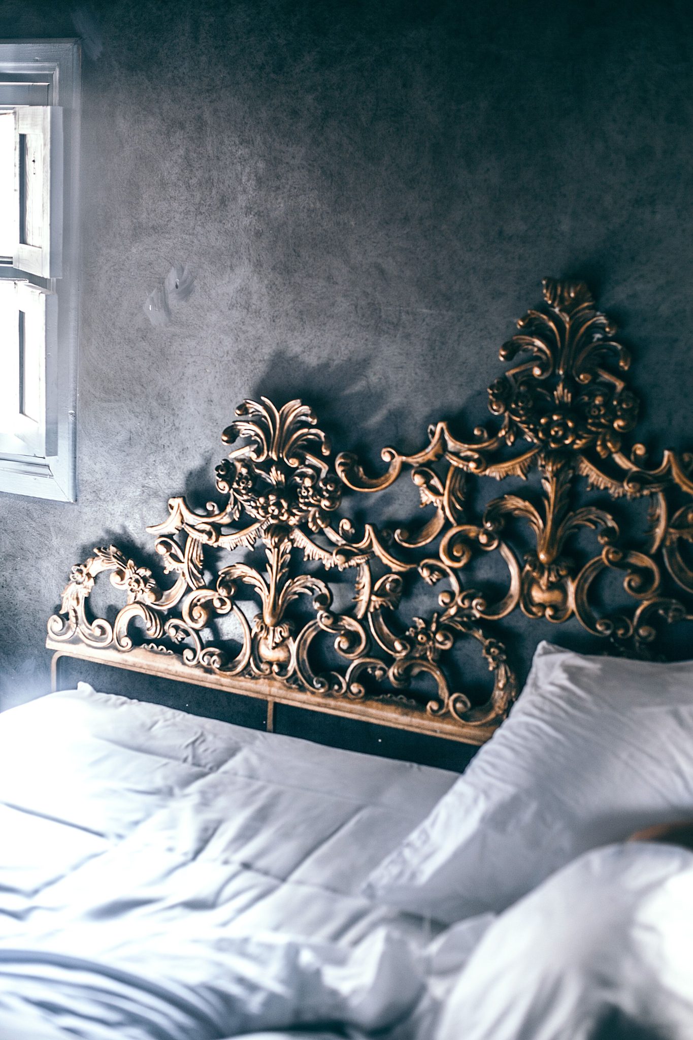 From above of comfortable unmade bed with white sheet and blanket and decorative carved elements on headboard