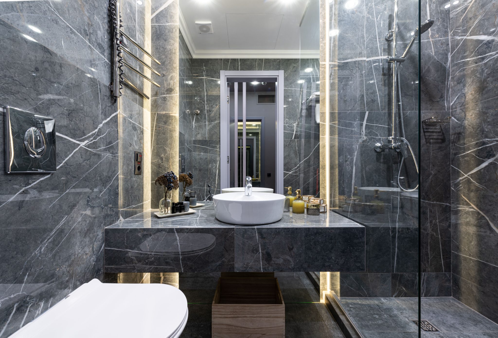 Interior of contemporary spacious bathroom with black tiled walls and shower cabin with white sink at mirror near ceramic bidet