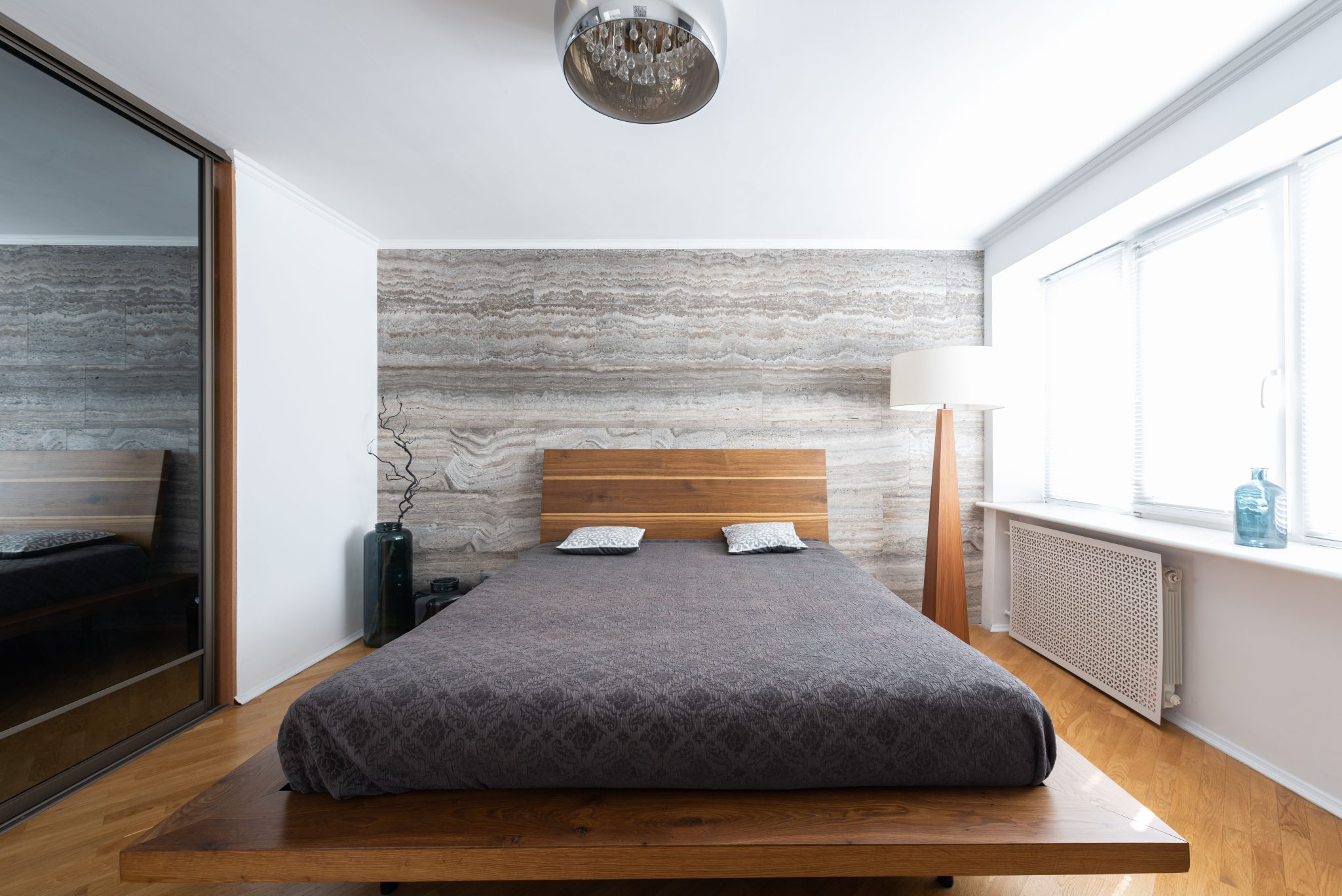 Interior of light modern flat with bed near lamps on floor and ceiling near vases with leafless sprig near mirror wall and window with windowsill