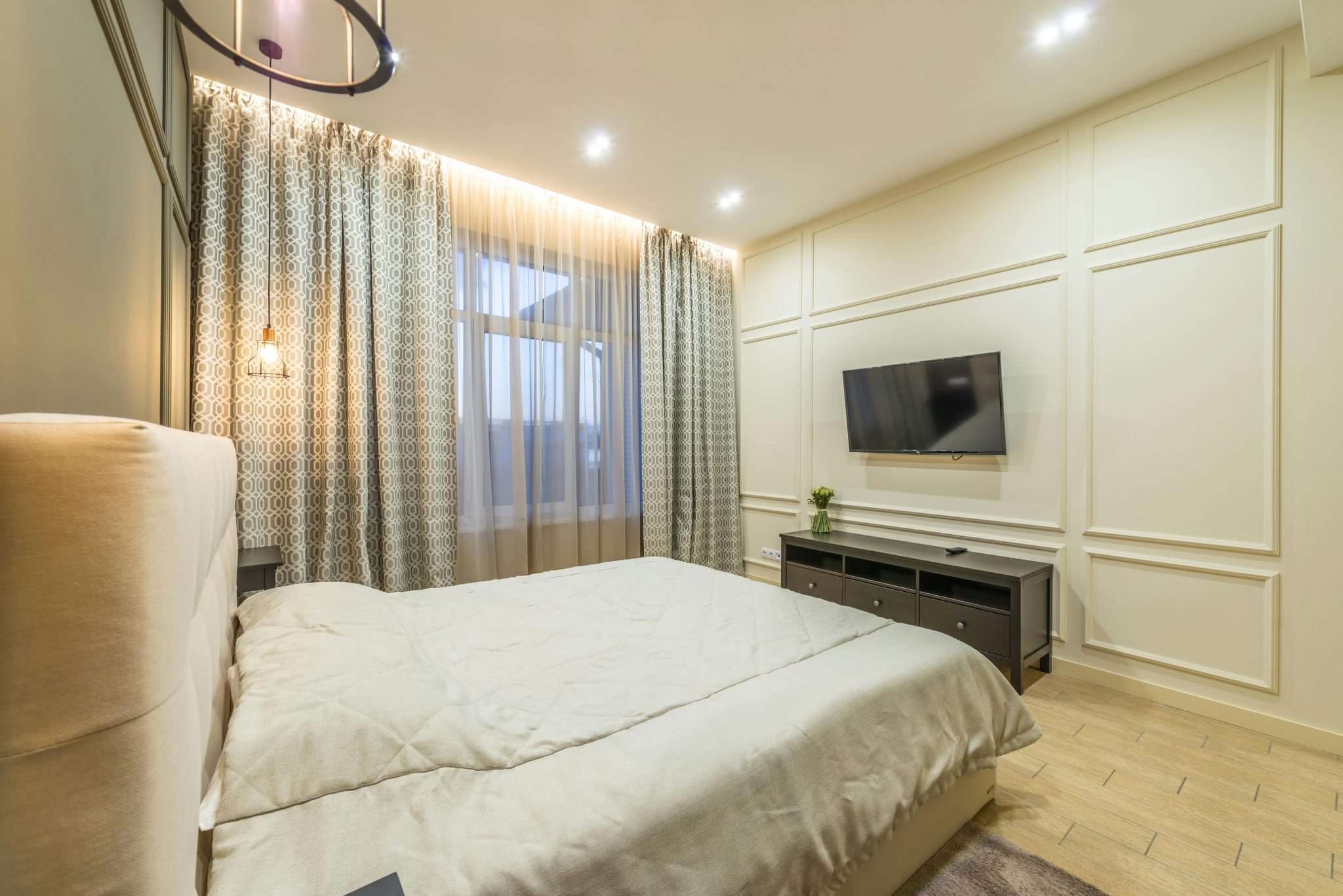 Interior of modern bedroom with comfortable bed and big window covered with curtains under luminous lights