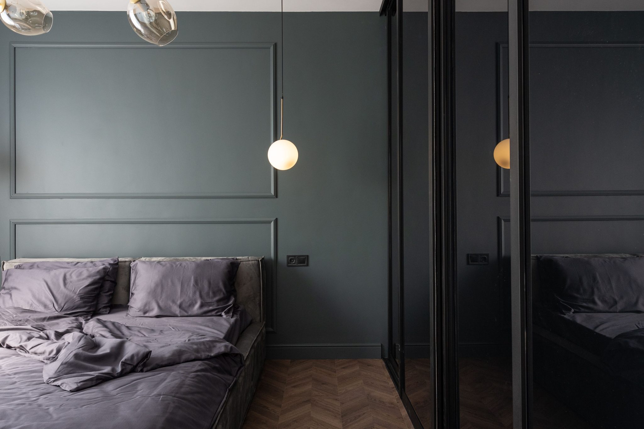 Interior of modern bedroom with shining lamp hanging above bed covered with gray bedclothes placed near cabinet