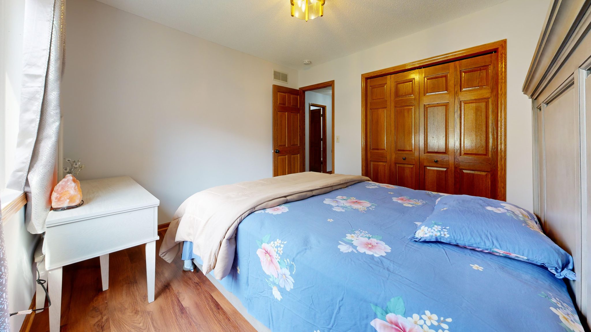 Inviting bedroom interior featuring blue floral bedding and wooden closet doors.