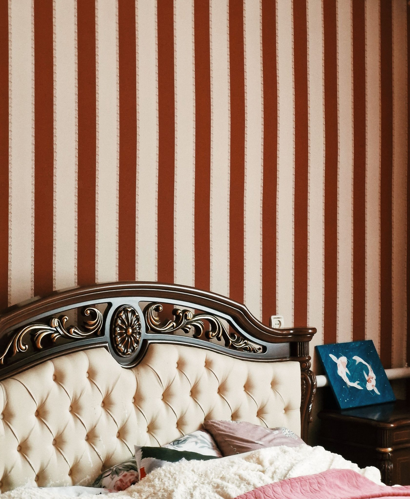 Luxurious bedroom featuring a carved wooden headboard and striped wallpaper for a classic look.