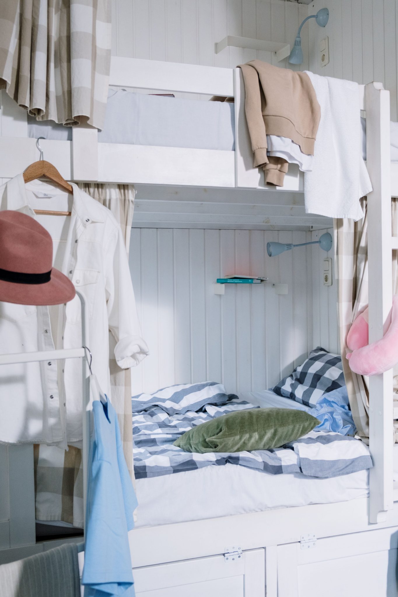 Neatly arranged dorm room featuring a stylish bunk bed with hanging clothes and vibrant decor.