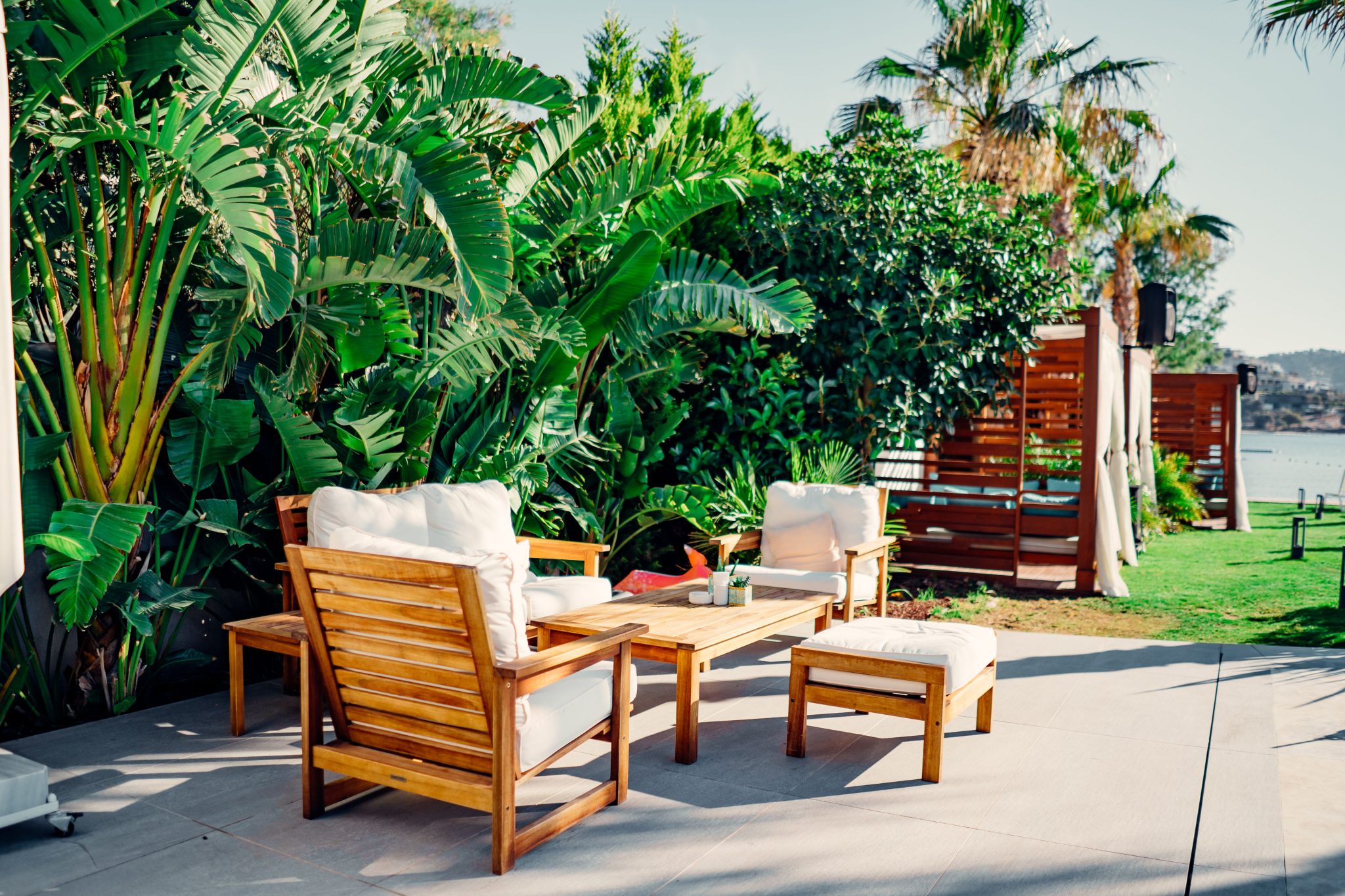 Relaxing outdoor patio with wooden furniture surrounded by lush greenery and tropical plants.