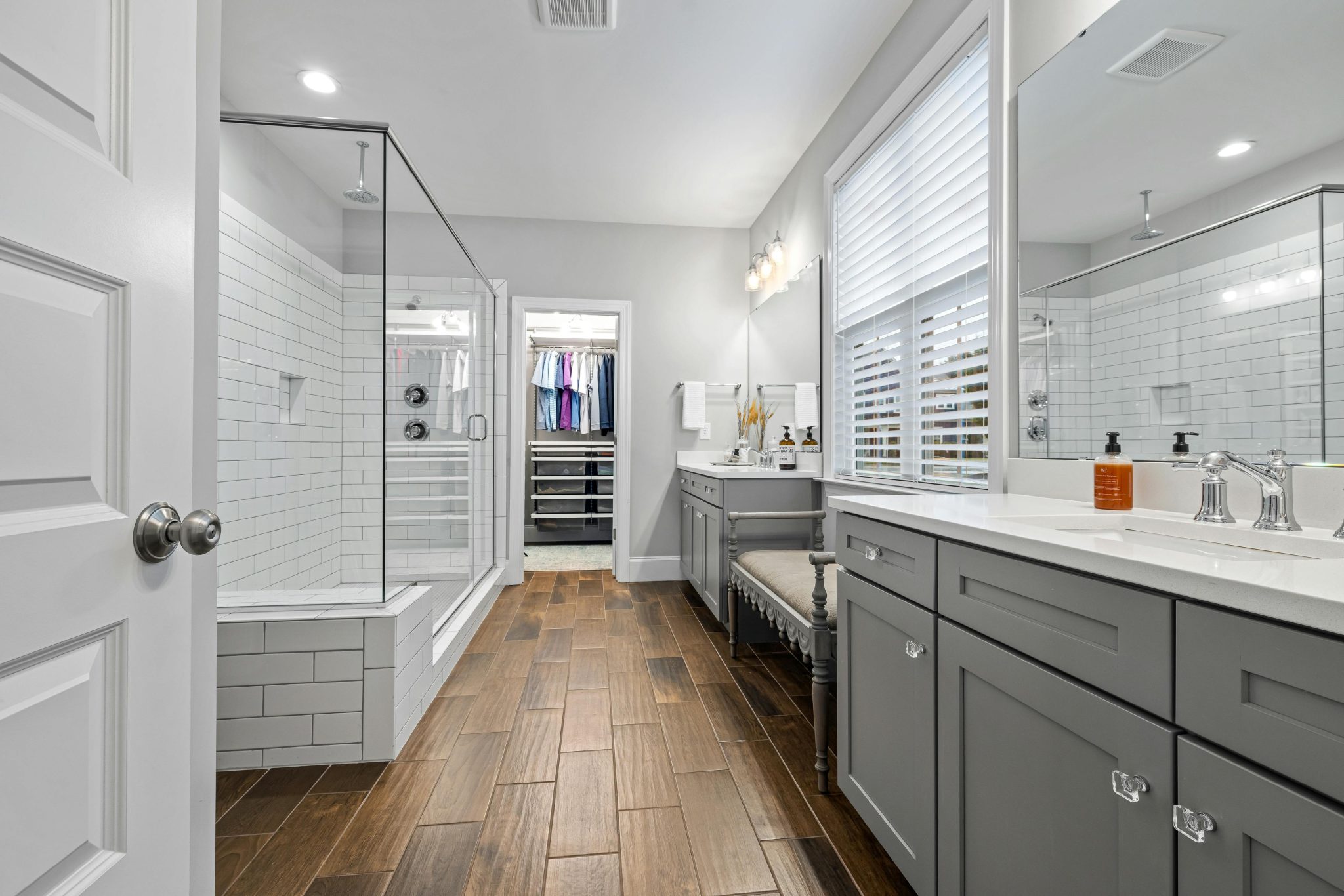 Spacious modern bathroom with glass shower, wooden flooring, and grey cabinets.