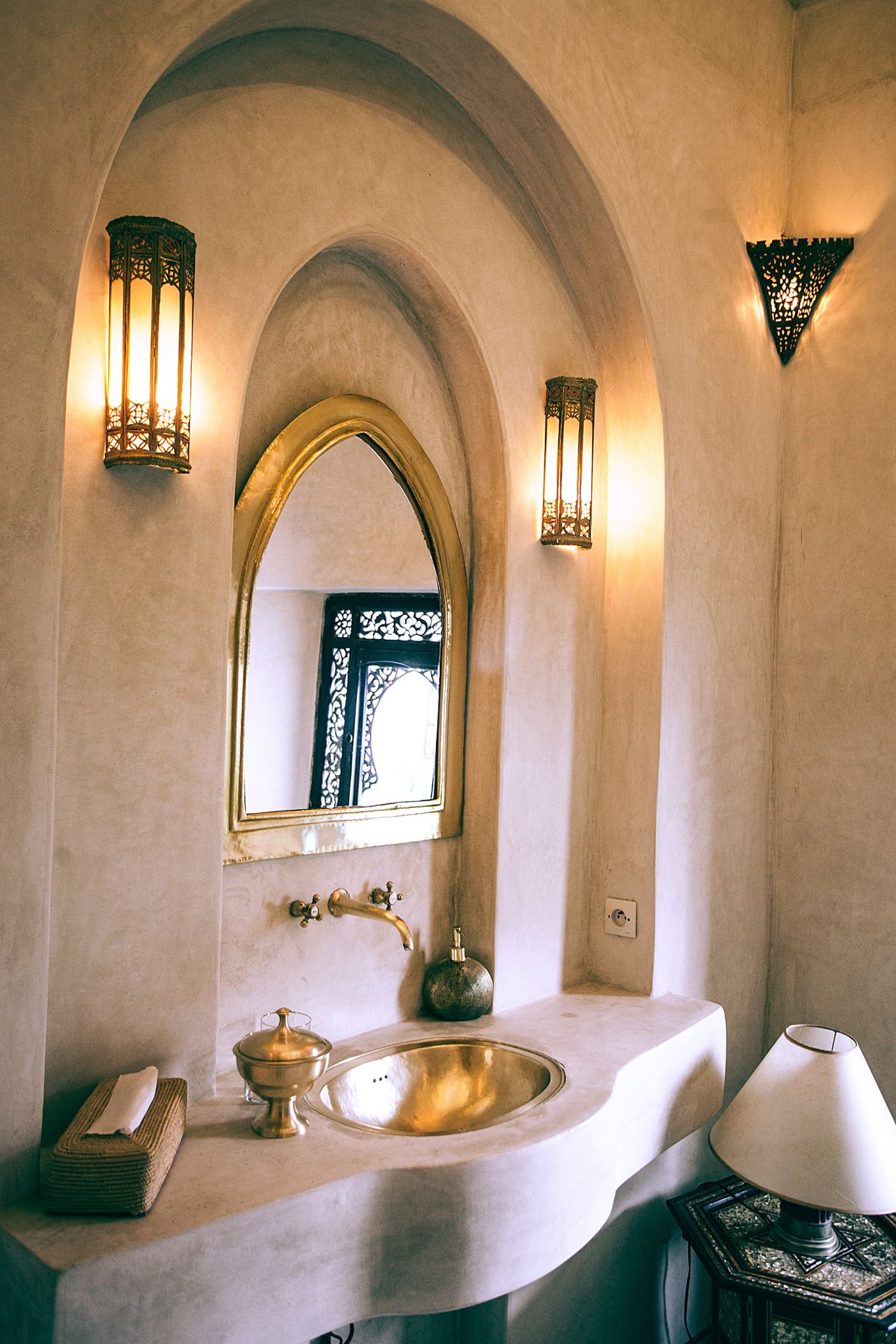 Stylish bathroom with golden faucet and sink under framed mirror and shiny lamps