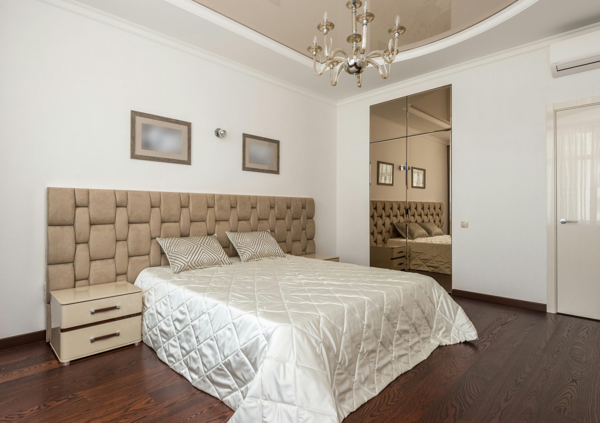 Stylish modern bedroom with plush headboard, chandelier, and mirrored closet doors.