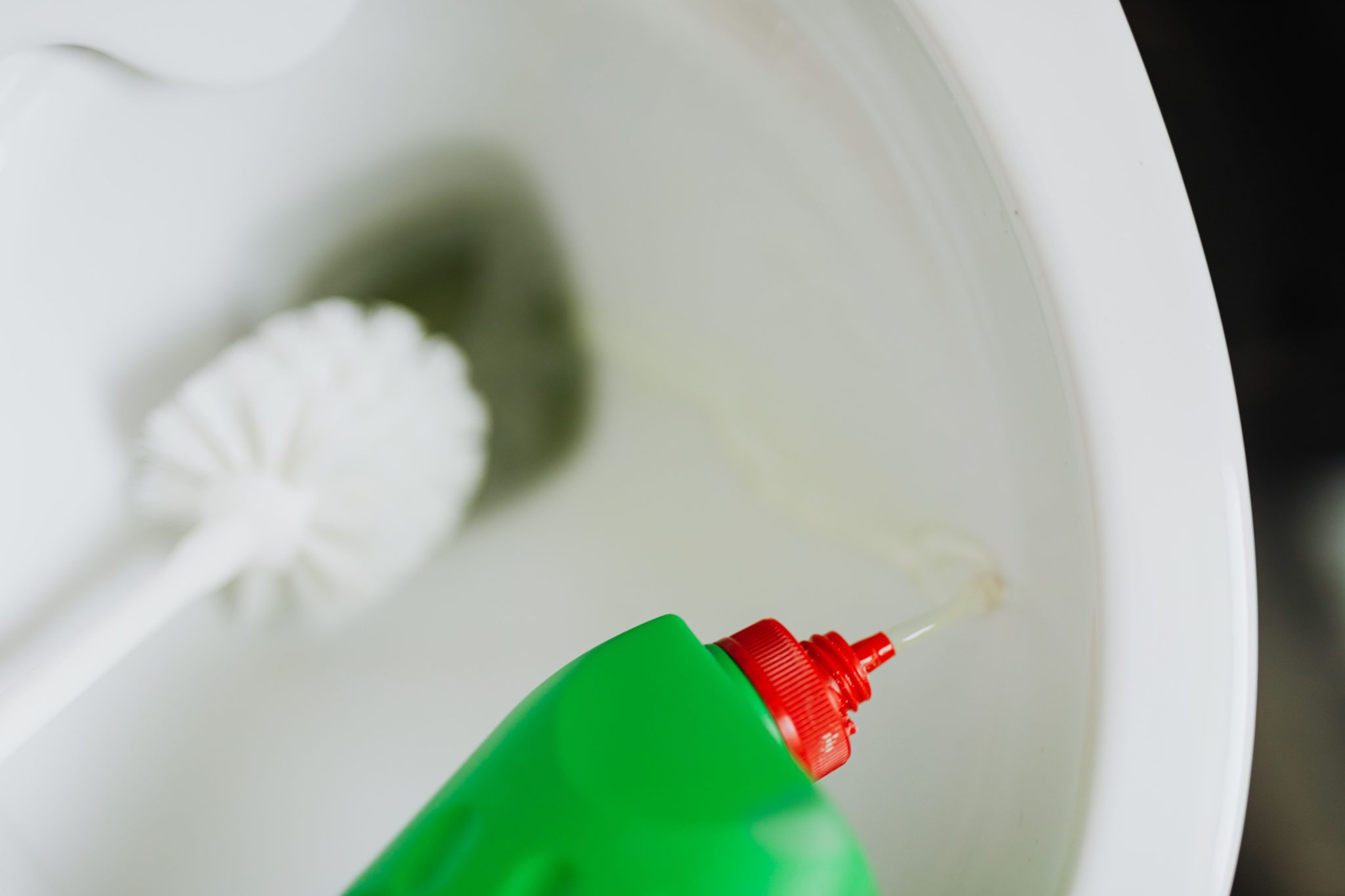 Top view of liquid detergent pouring from green plastic bottle in toilet bowl with toilet brush