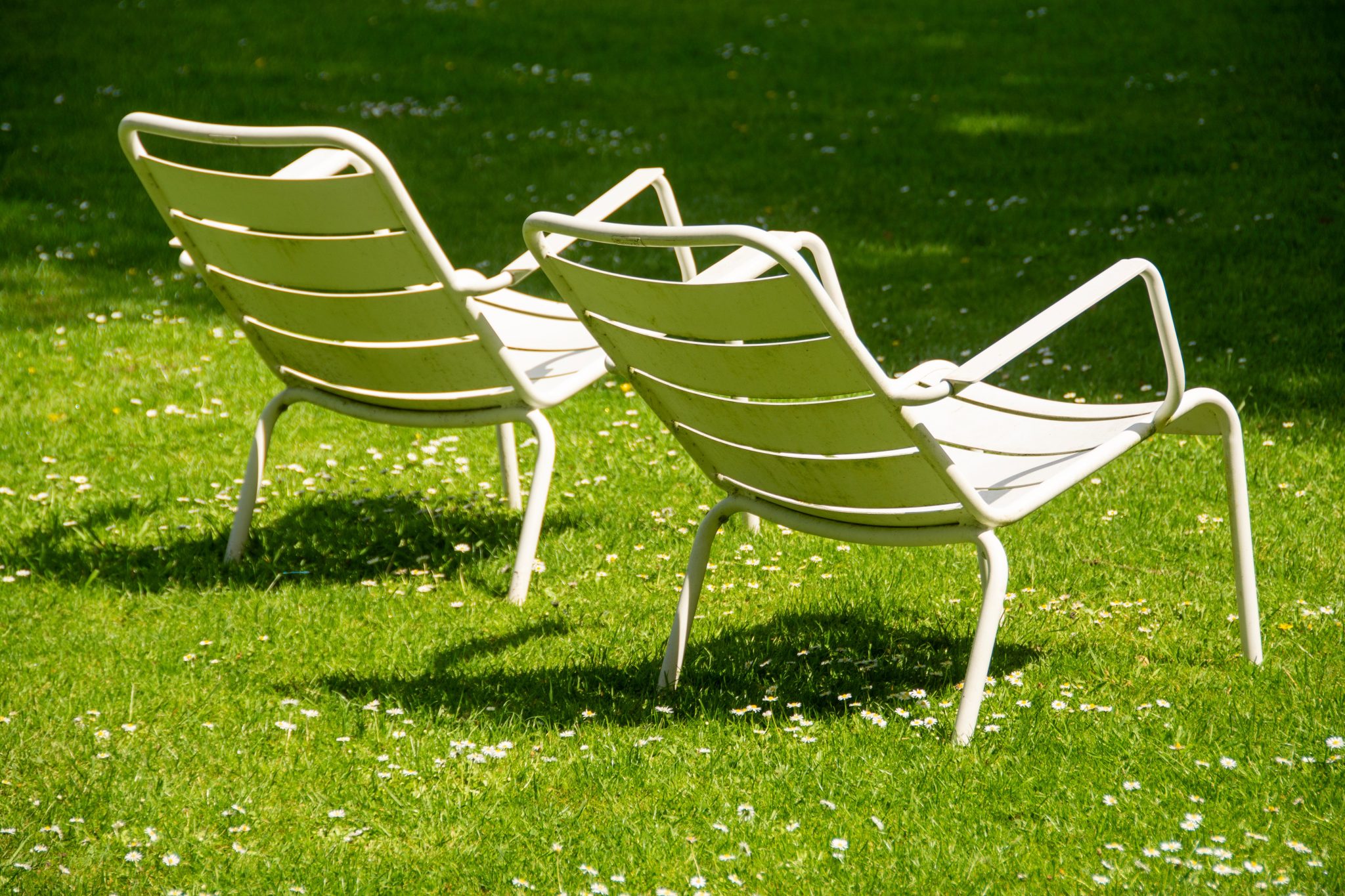 Two white metal chairs on a vibrant green lawn under sunlight.