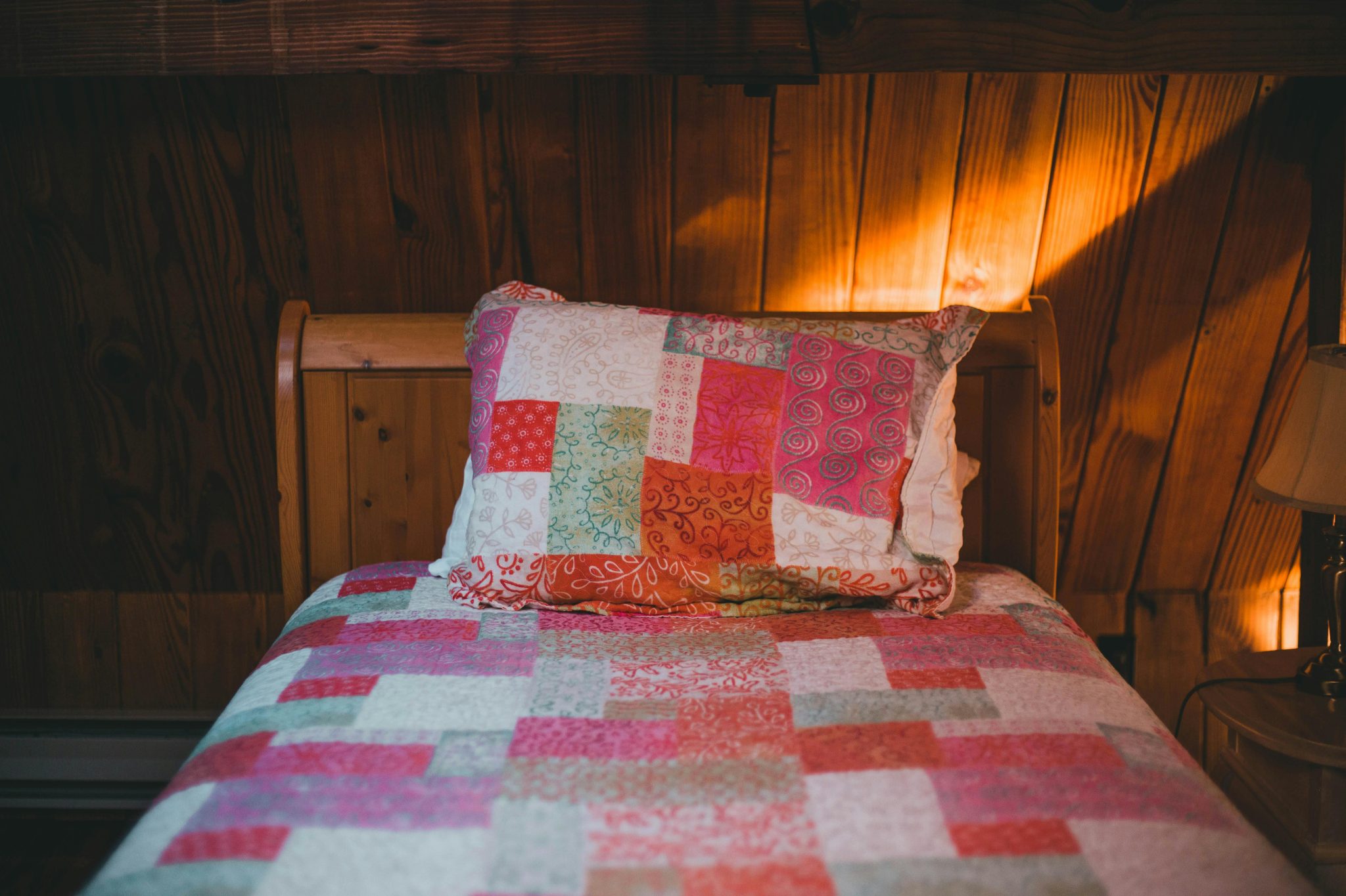 Warm and inviting wooden cabin bedroom featuring a colorful patchwork quilt and pillow.