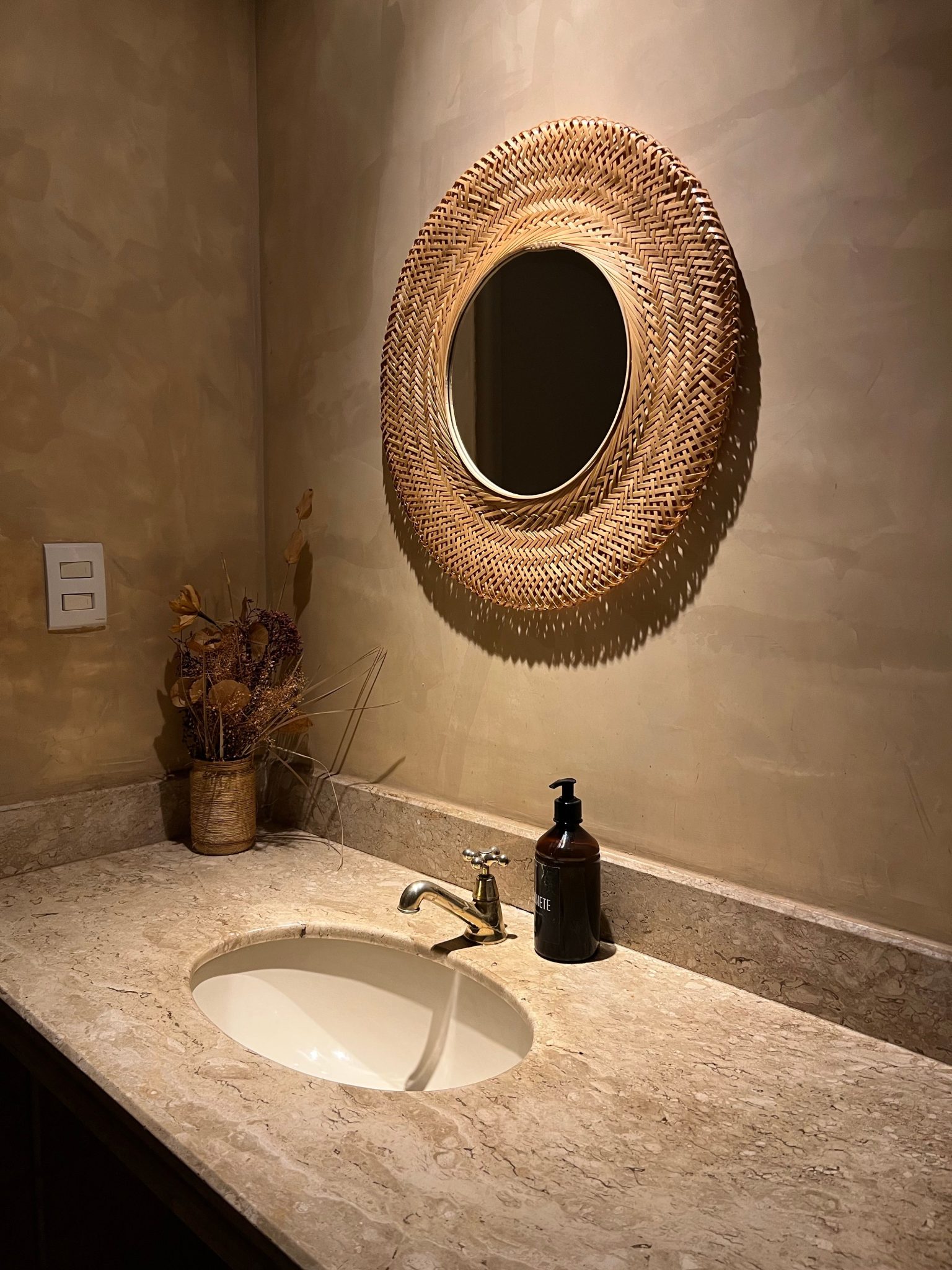 Warm-toned bathroom with wicker mirror and marble sink for a stylish look.