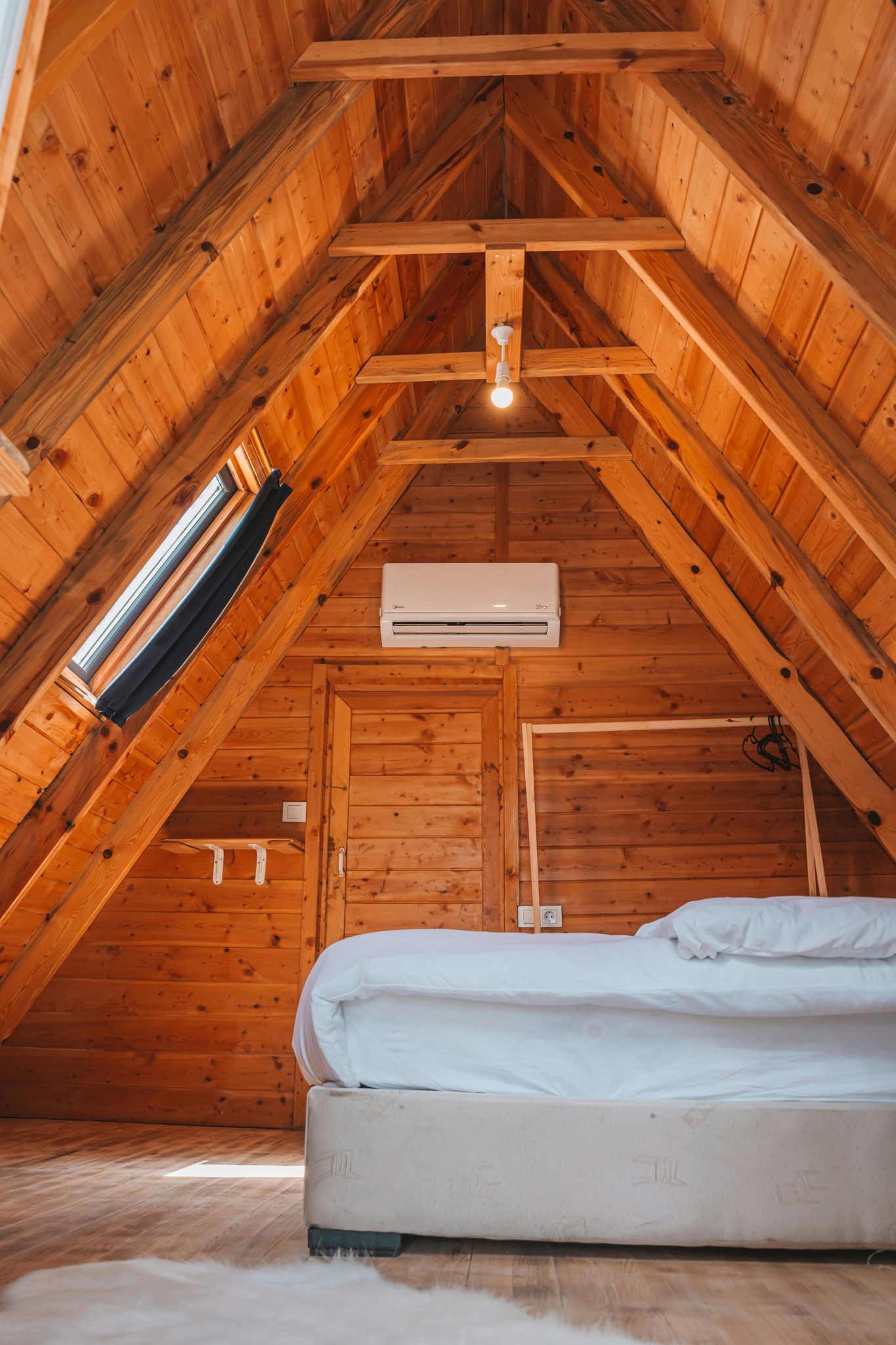 Warm wooden attic bedroom with bed and natural light in Kemer, Türkiye.
