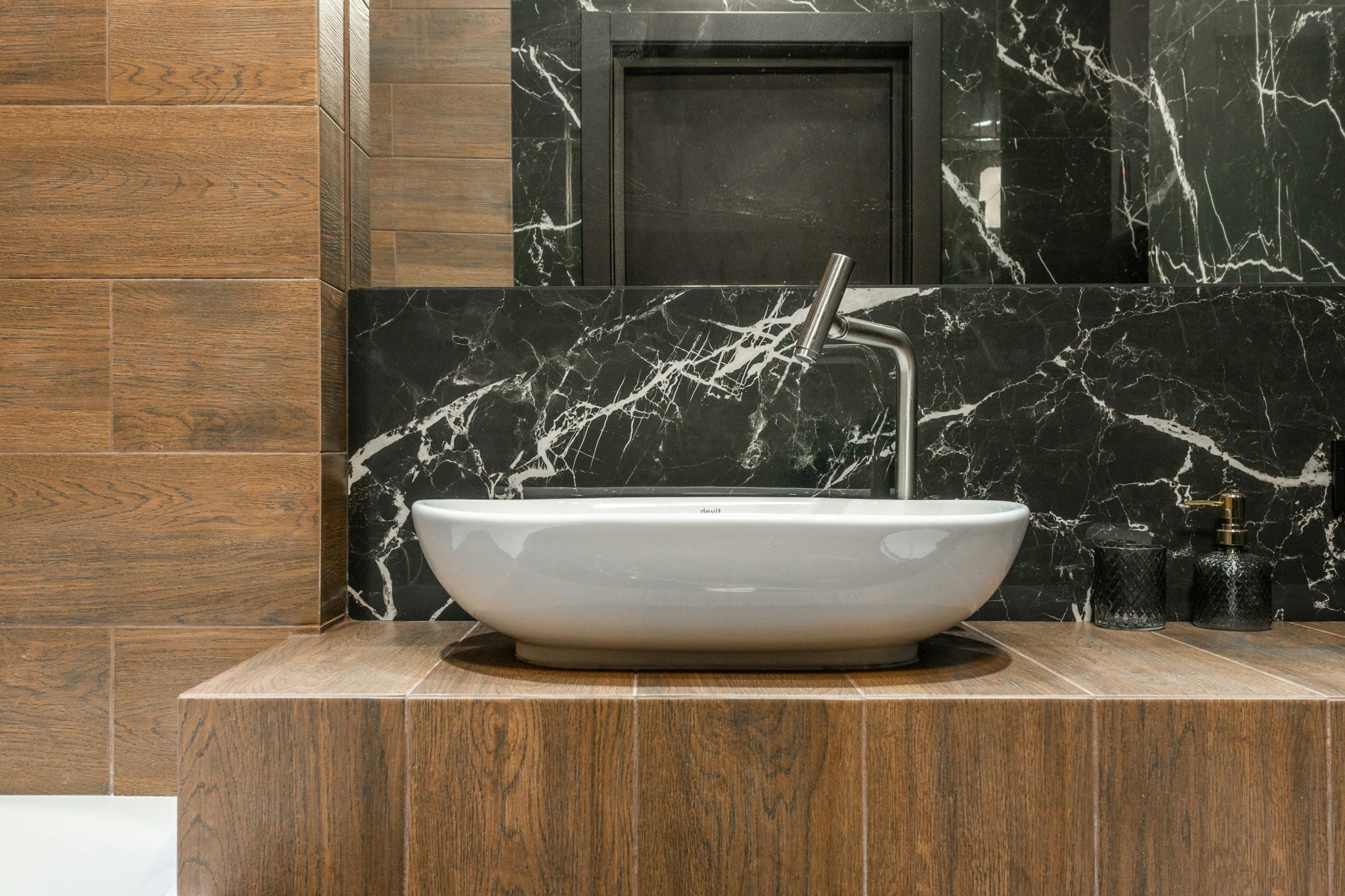 White sink and faucet in stylish modern bathroom with marble and wood look tiles