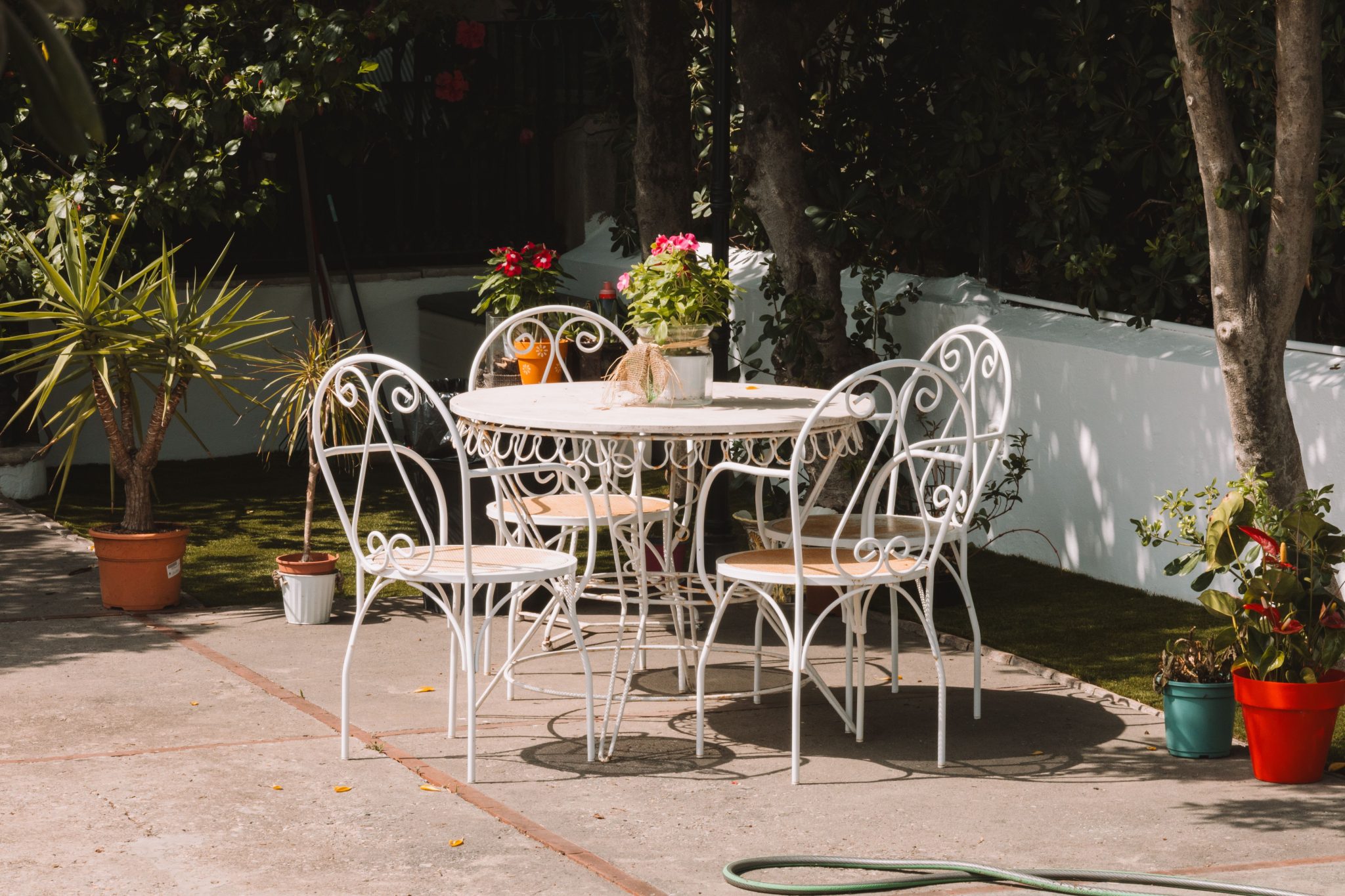 White wrought iron furniture surrounded by plants in a sunny café garden.