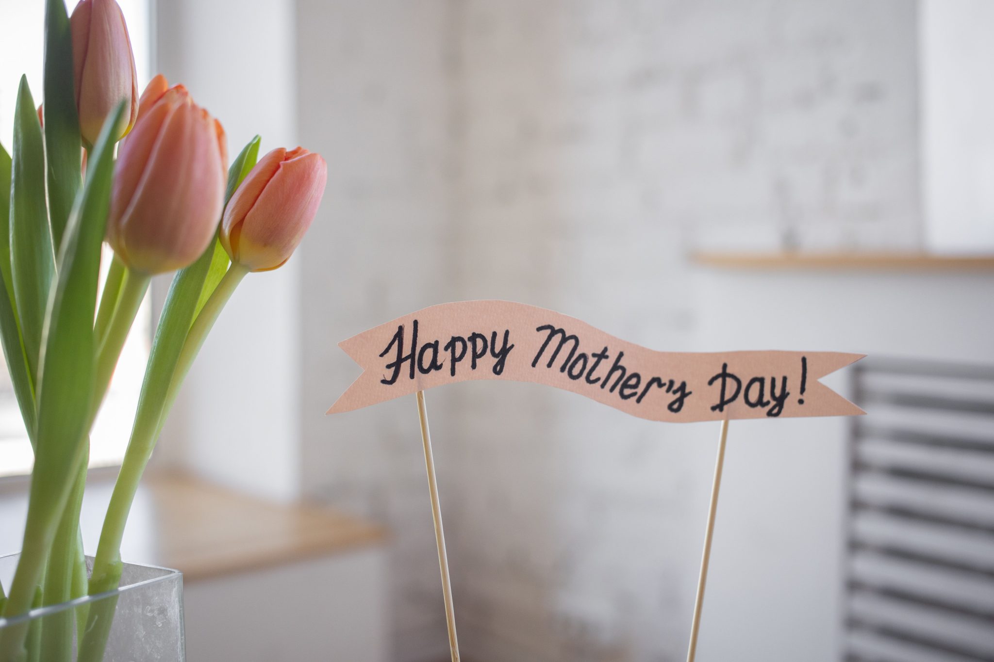 A beautiful arrangement of pink tulips with a 'Happy Mother's Day' sign indoors, perfect for celebration.
