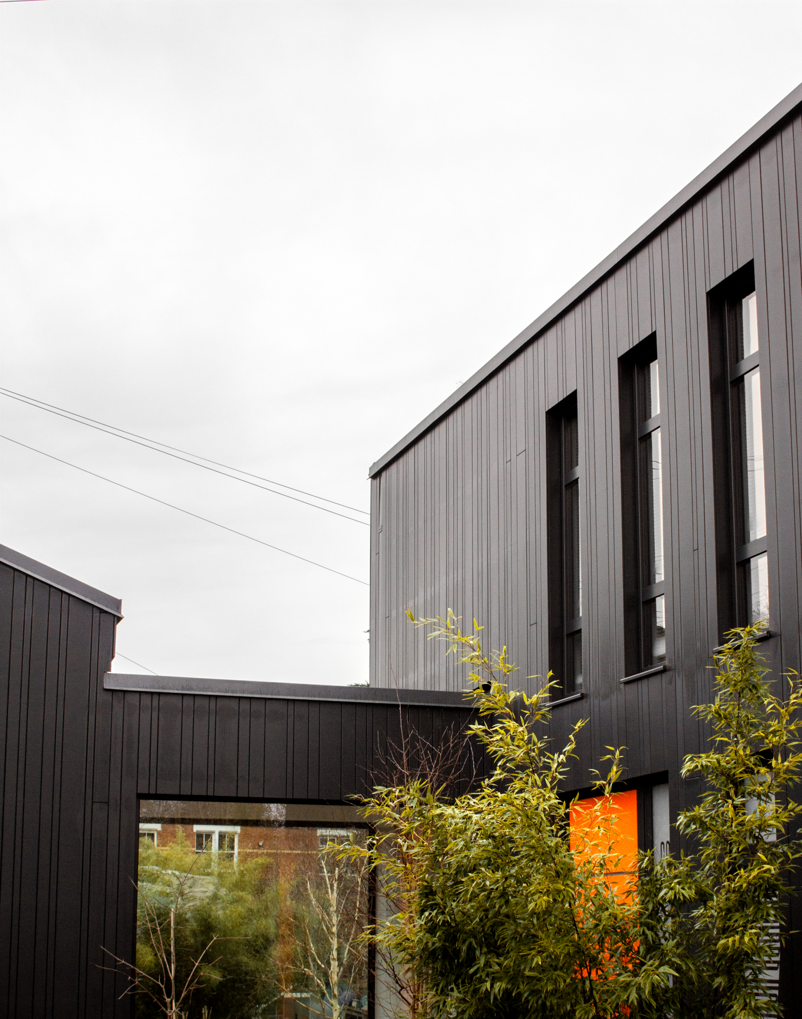 A contemporary black house with bold architecture and a striking orange door on an overcast day.
