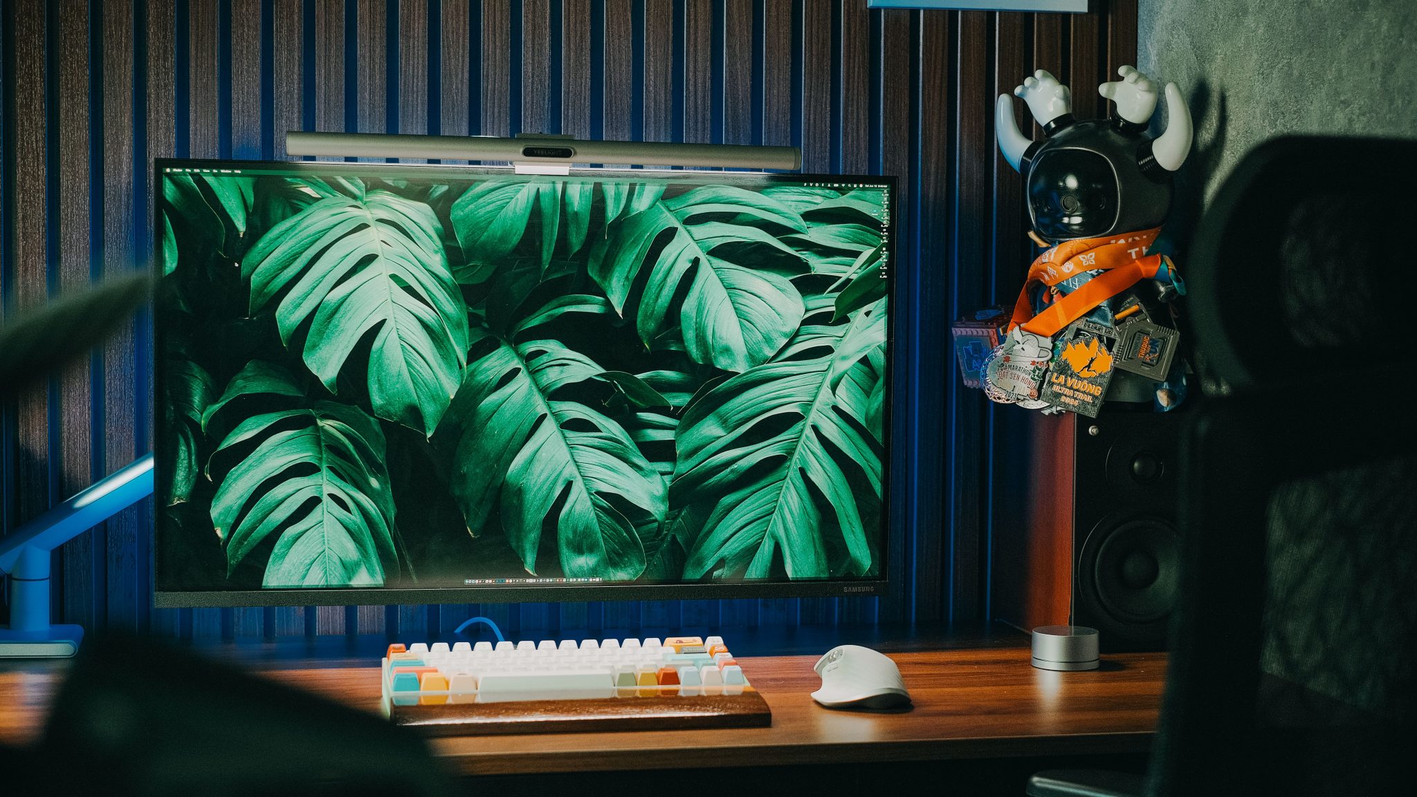A modern home office setup with a PC, keyboard, and Monstera leaves wallpaper.