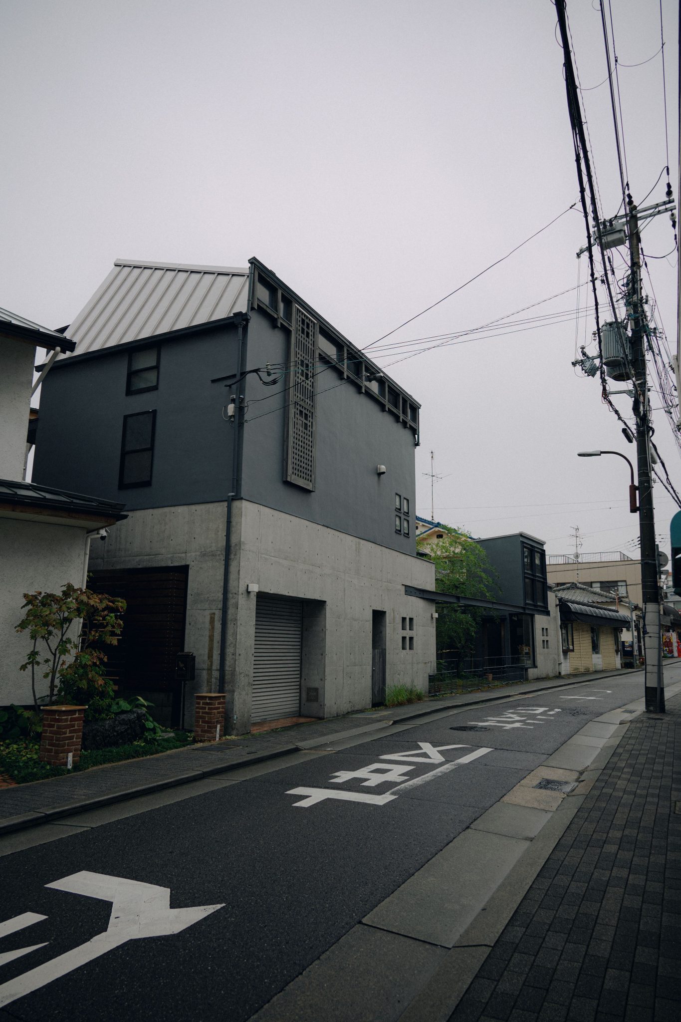 A quiet residential street featuring modern, minimalist architecture with concrete and dark facade.