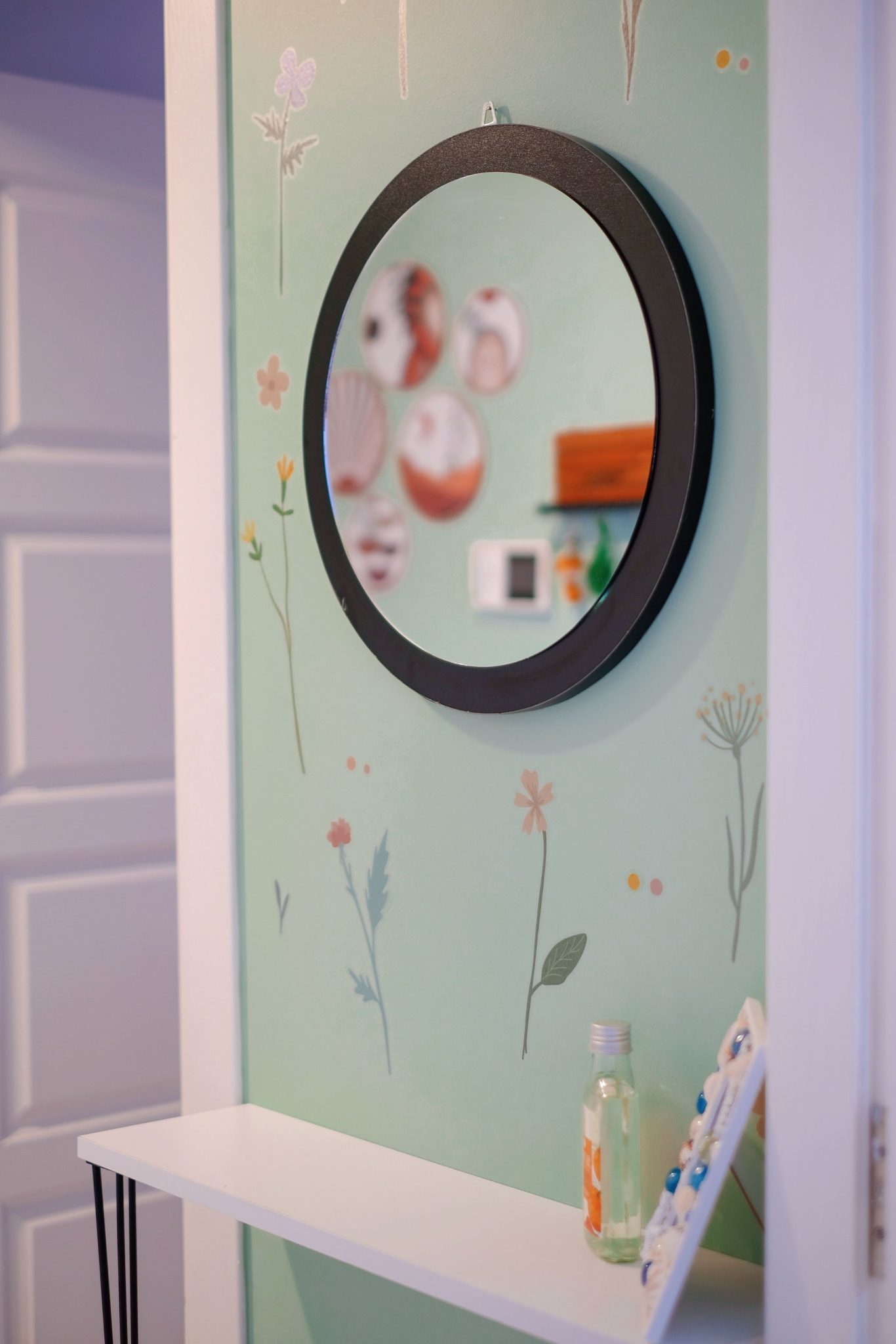 A round mirror on a pastel green floral wall decorates a modern home interior.