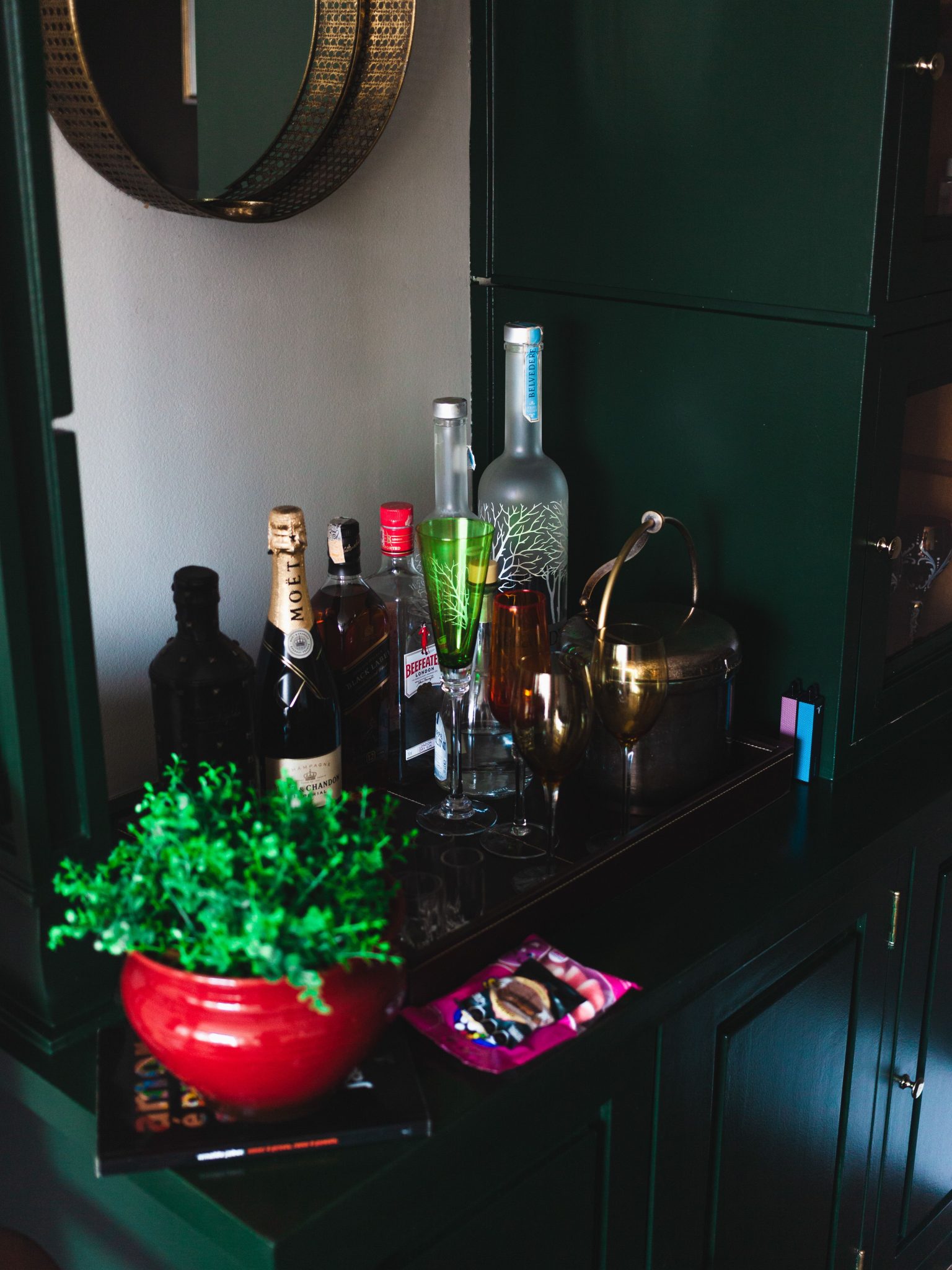 A stylish home bar setup featuring various liquor bottles, glassware, and a decorative plant.