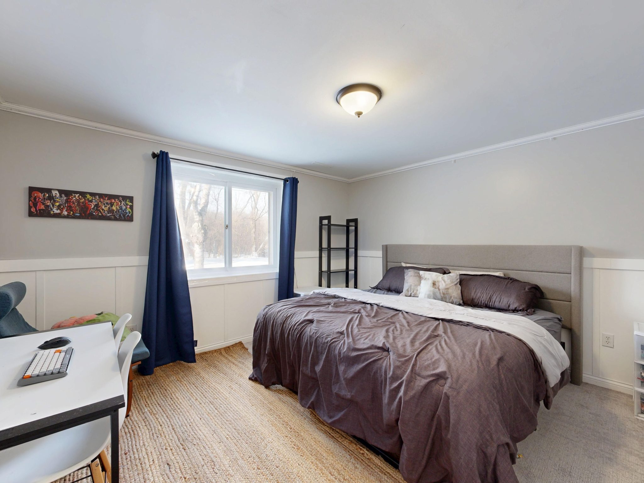 A stylish modern bedroom with a large bed, desk, and window with natural lighting.