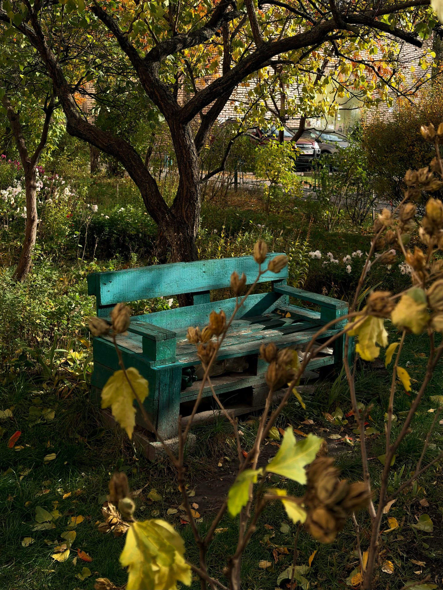 A weathered green bench sits in an autumn garden.