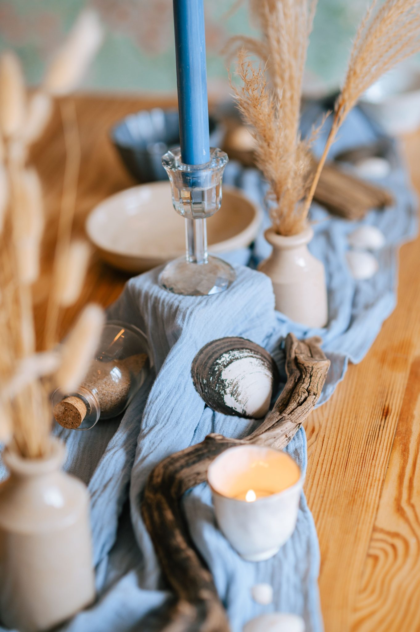 Aesthetic coastal-themed table setup featuring candles, driftwood, and elegant decor.