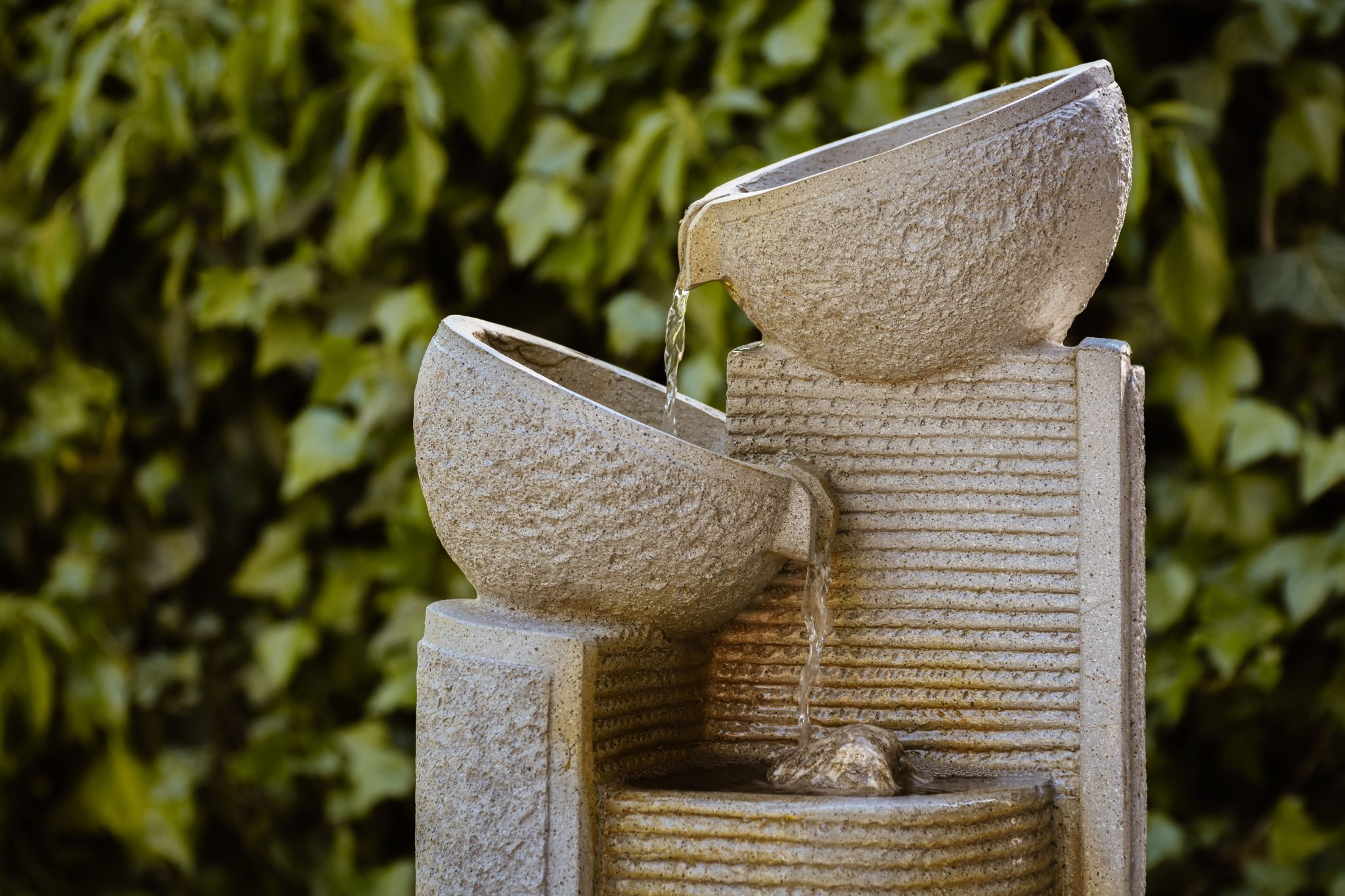 An elegant stone fountain with cascading water in a lush garden setting, providing a tranquil atmosphere.