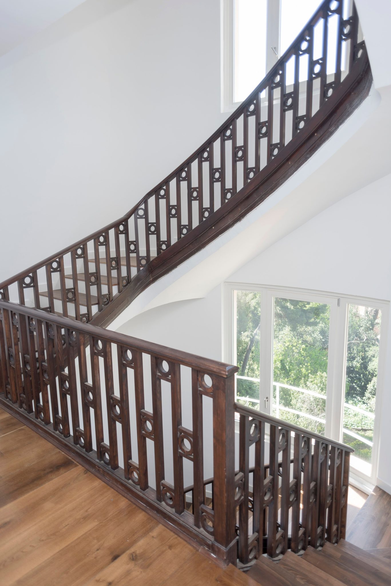 Beautiful wooden staircase with intricate railing in a sunlit interior space.