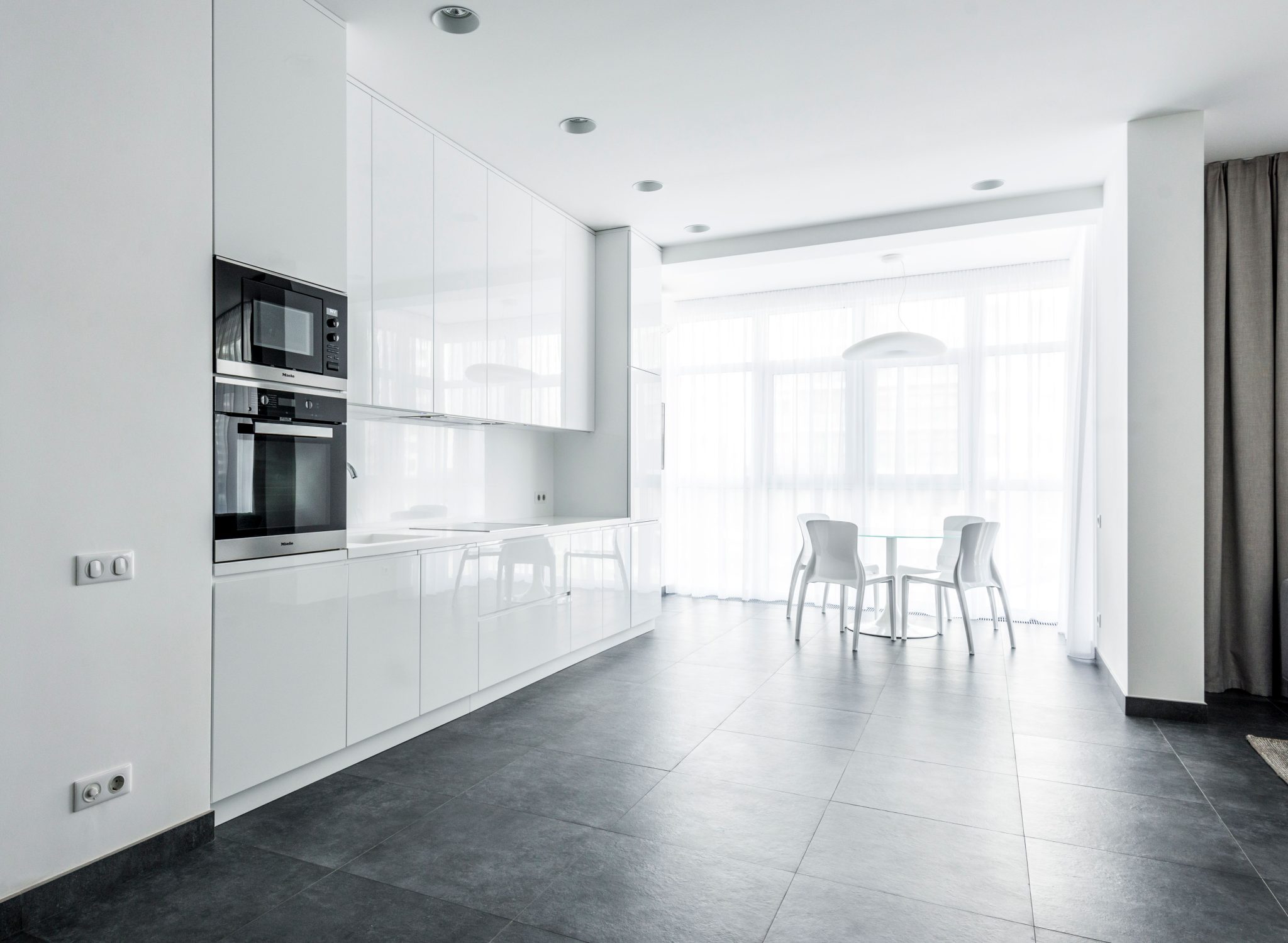 Bright minimalist kitchen featuring sleek white cabinetry and dining space.