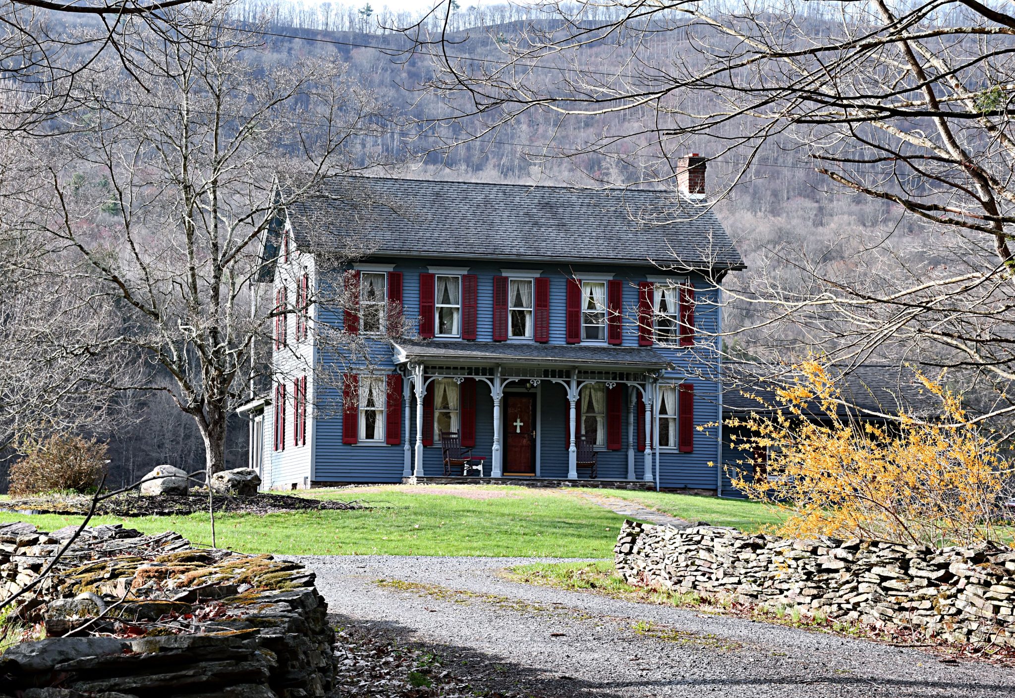 Charming historic house with red shutters, nestled in a scenic rural mountain landscape.