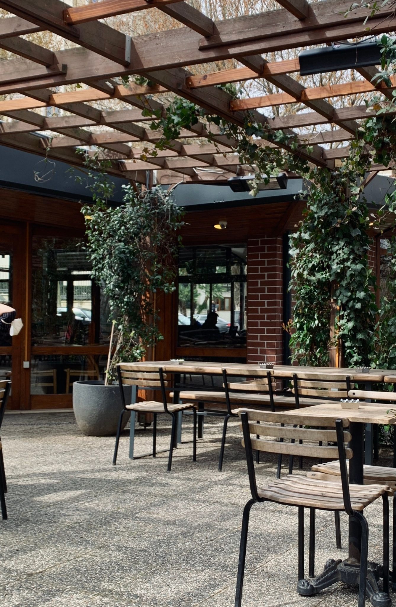 Charming outdoor patio with wooden furniture, lush plants, and natural light filtering through a trellis.