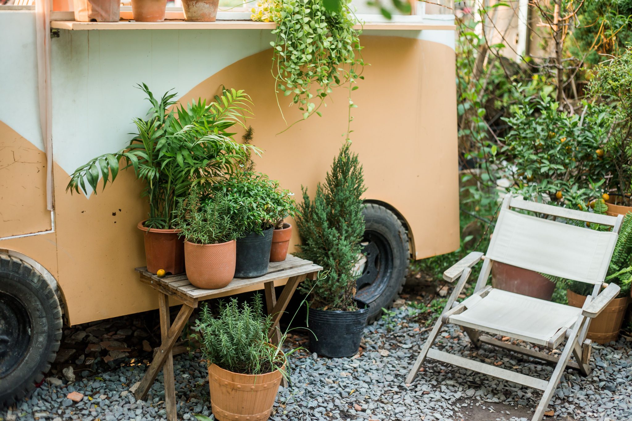 Charming patio space featuring potted plants and a comfortable chair beside a vintage trailer.